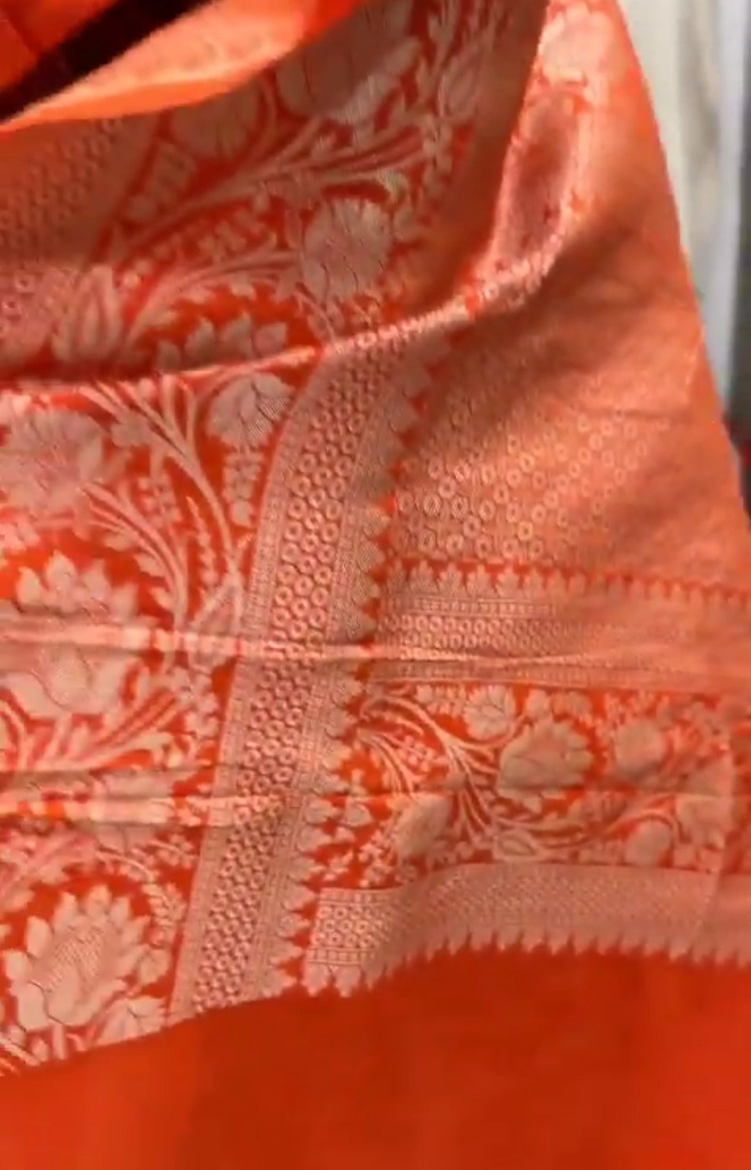 A vibrant orange Banarasi Katan silk saree with multi-colored Tilfi Meenakari floral motifs and an elaborate gold zari border.