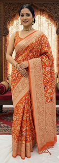 A vibrant orange Banarasi Katan silk saree with multi-colored Tilfi Meenakari floral motifs and an elaborate gold zari border.
