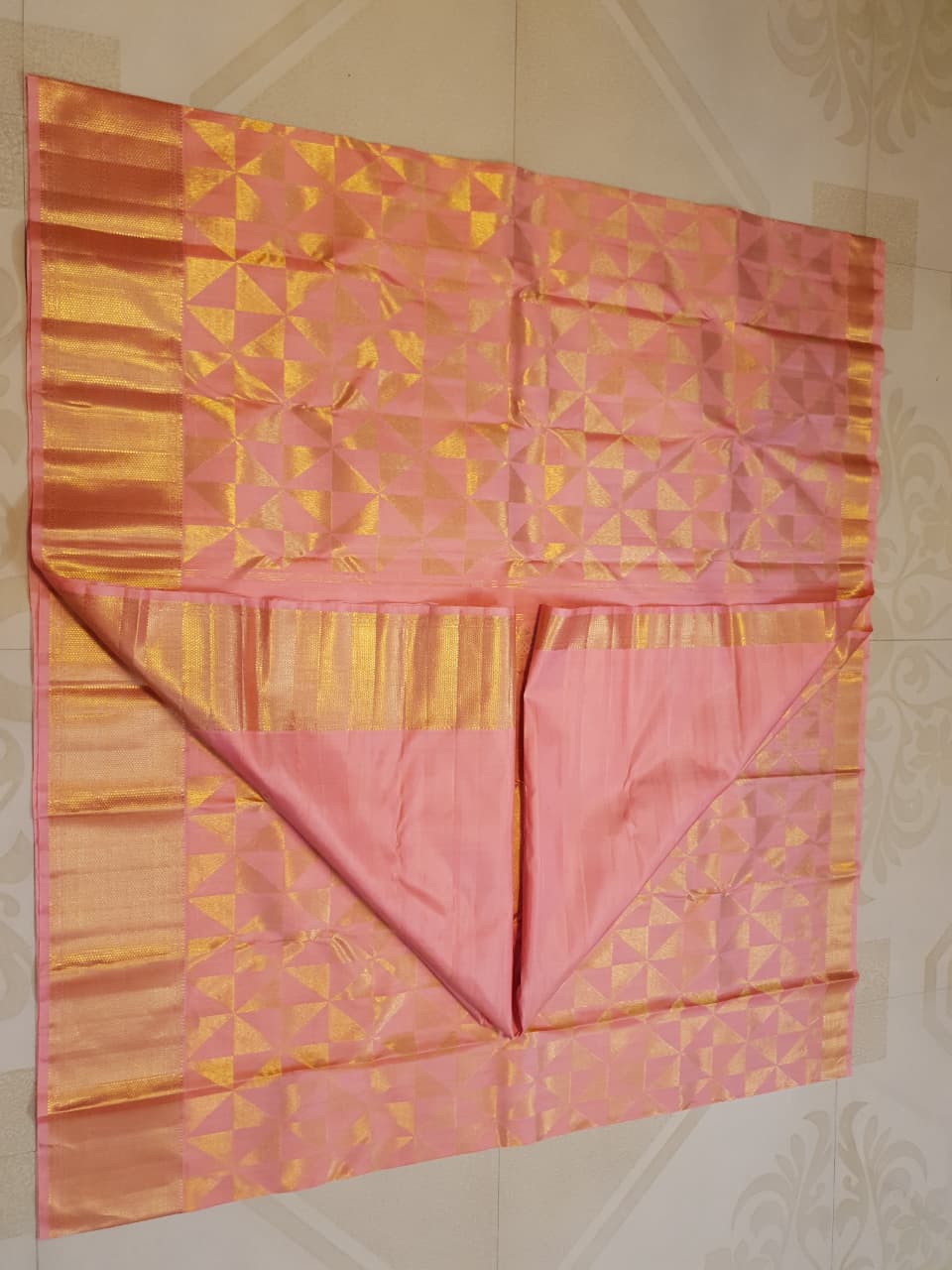 Peach Kanchipuram Handloom 2G Gold Pattu Silk Saree with geometric triangle patterns and a heavy gold border, set against a traditional palace courtyard.