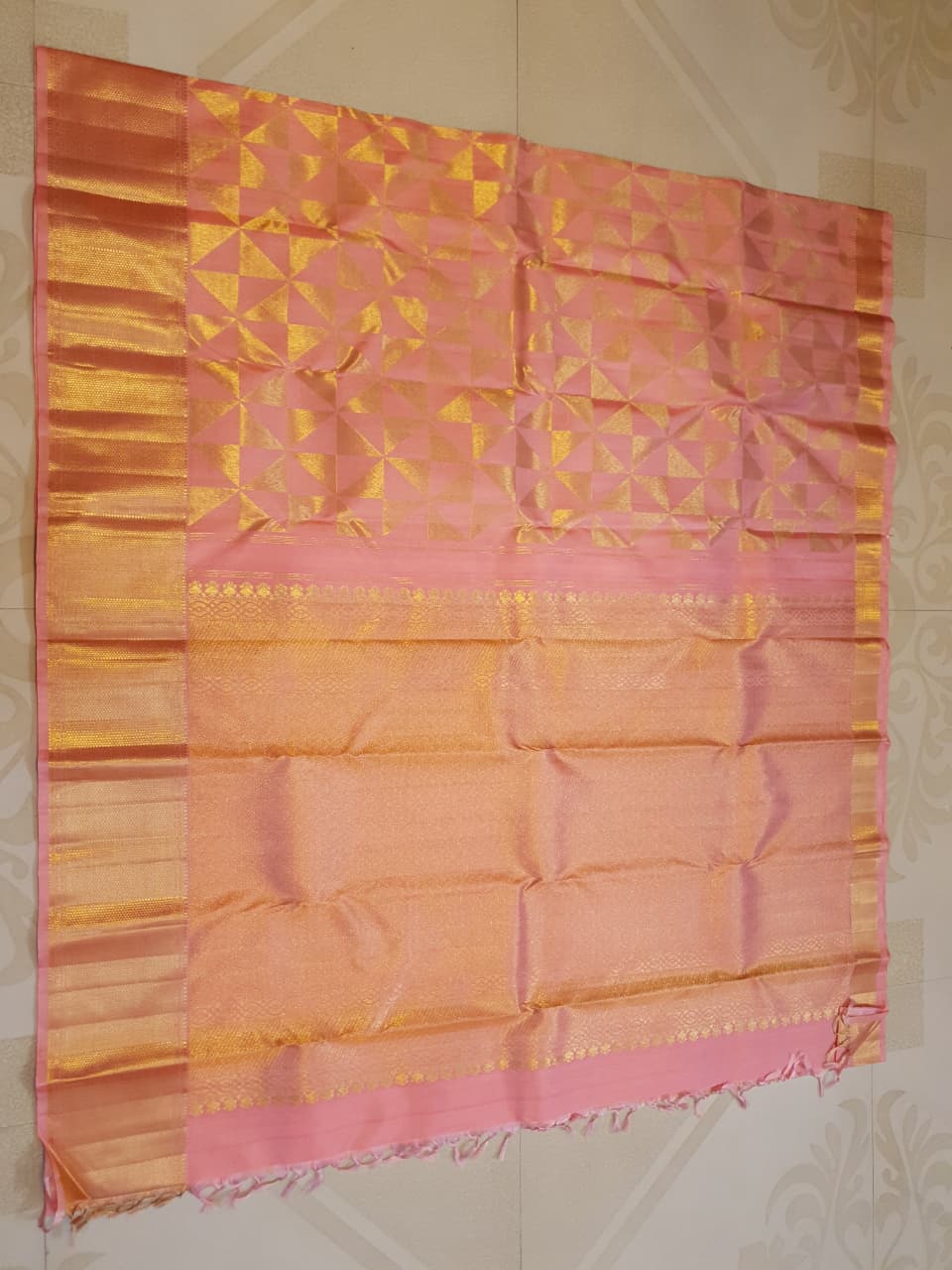 Peach Kanchipuram Handloom 2G Gold Pattu Silk Saree with geometric triangle patterns and a heavy gold border, set against a traditional palace courtyard.