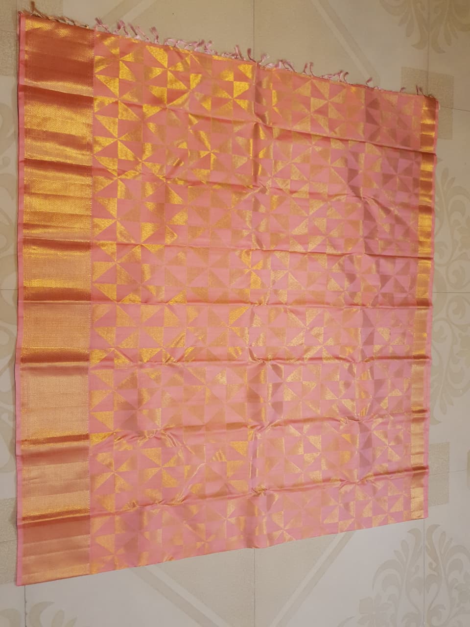 Peach Kanchipuram Handloom 2G Gold Pattu Silk Saree with geometric triangle patterns and a heavy gold border, set against a traditional palace courtyard.