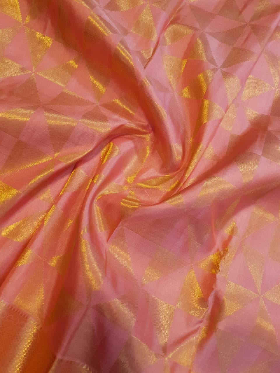 Peach Kanchipuram Handloom 2G Gold Pattu Silk Saree with geometric triangle patterns and a heavy gold border, set against a traditional palace courtyard.
