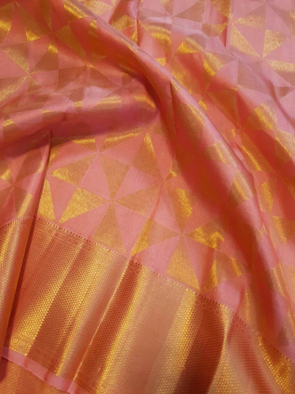 Peach Kanchipuram Handloom 2G Gold Pattu Silk Saree with geometric triangle patterns and a heavy gold border, set against a traditional palace courtyard.
