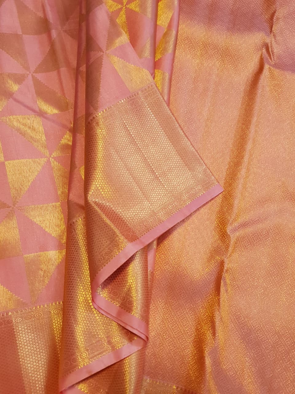 Peach Kanchipuram Handloom 2G Gold Pattu Silk Saree with geometric triangle patterns and a heavy gold border, set against a traditional palace courtyard.