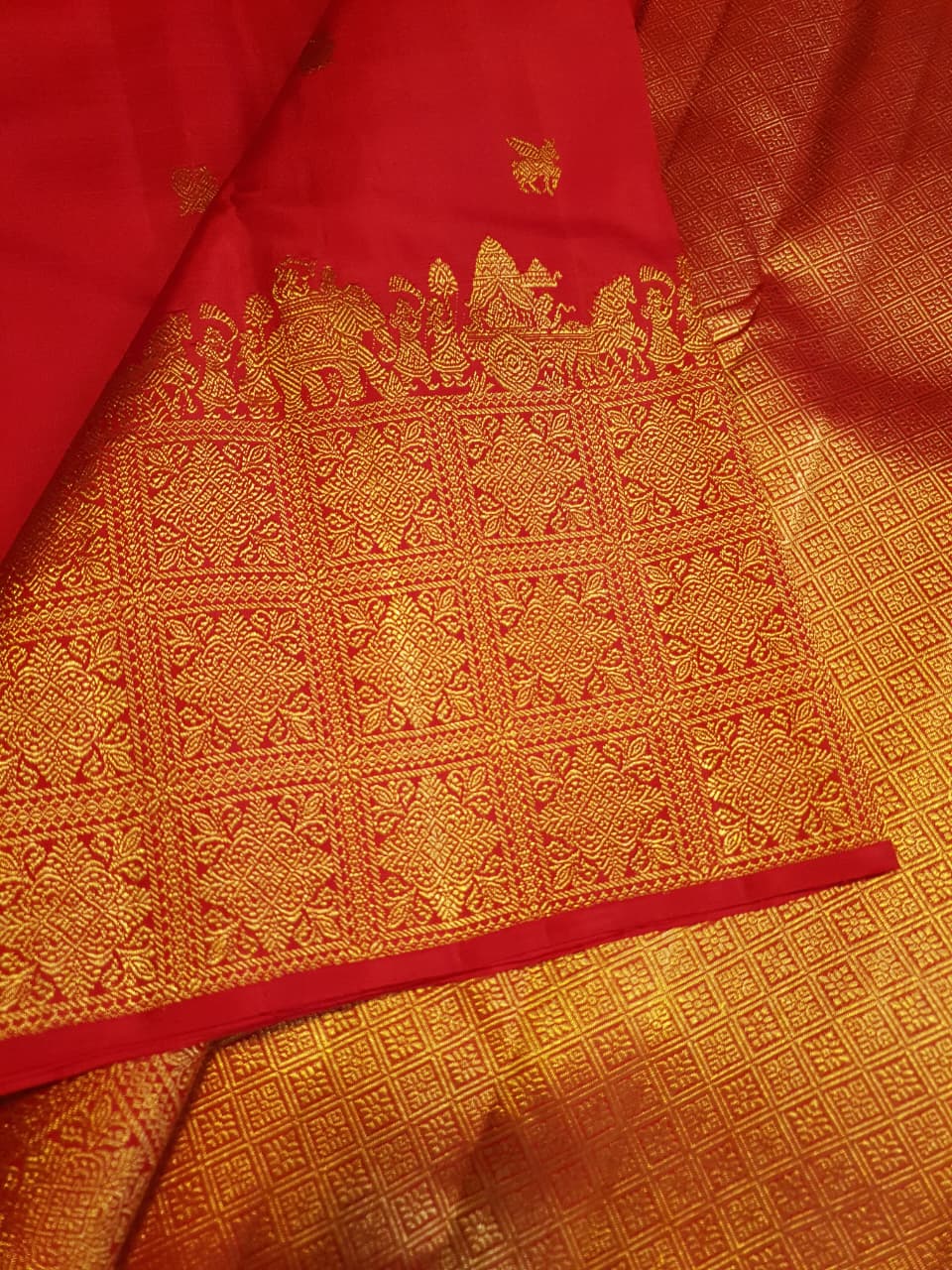 A close-up view of a premium 2G Kanjivaram pattu silk saree, highlighting the authentic Silk Mark tag, vibrant red fabric, and detailed gold zari work on the border and body.