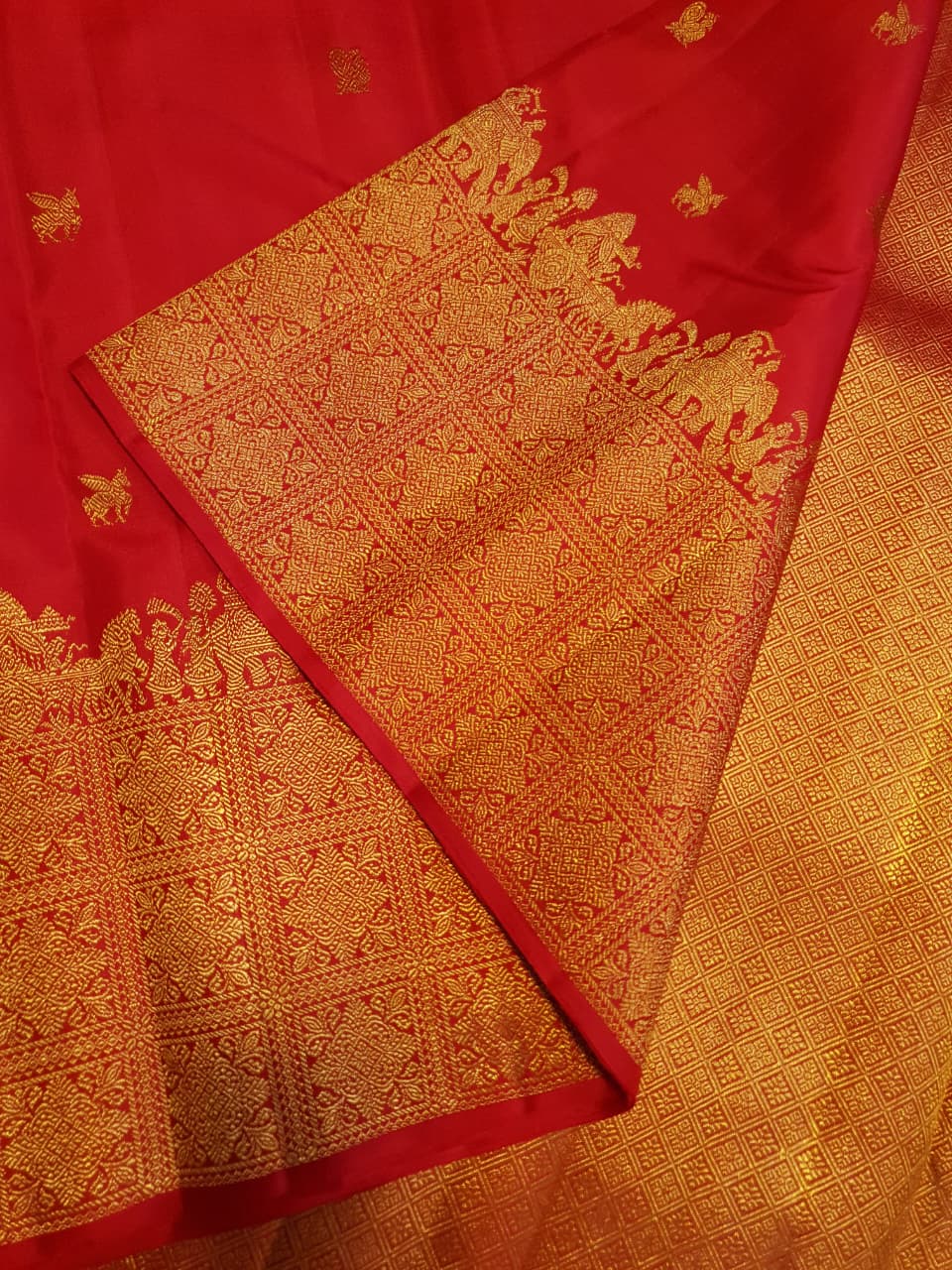 A close-up view of a premium 2G Kanjivaram pattu silk saree, highlighting the authentic Silk Mark tag, vibrant red fabric, and detailed gold zari work on the border and body.