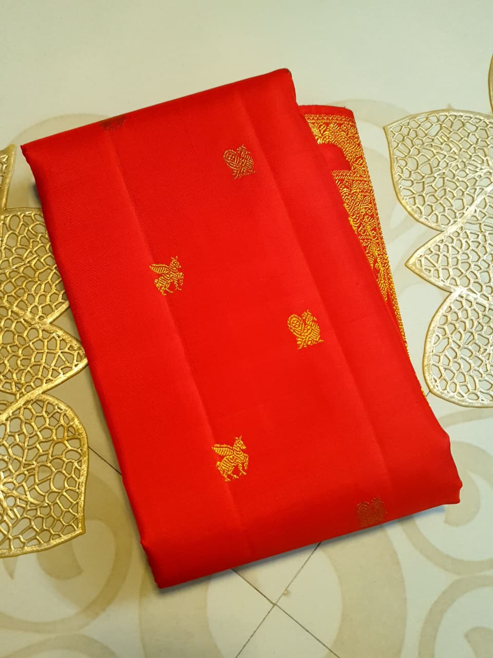 A close-up view of a premium 2G Kanjivaram pattu silk saree, highlighting the authentic Silk Mark tag, vibrant red fabric, and detailed gold zari work on the border and body.