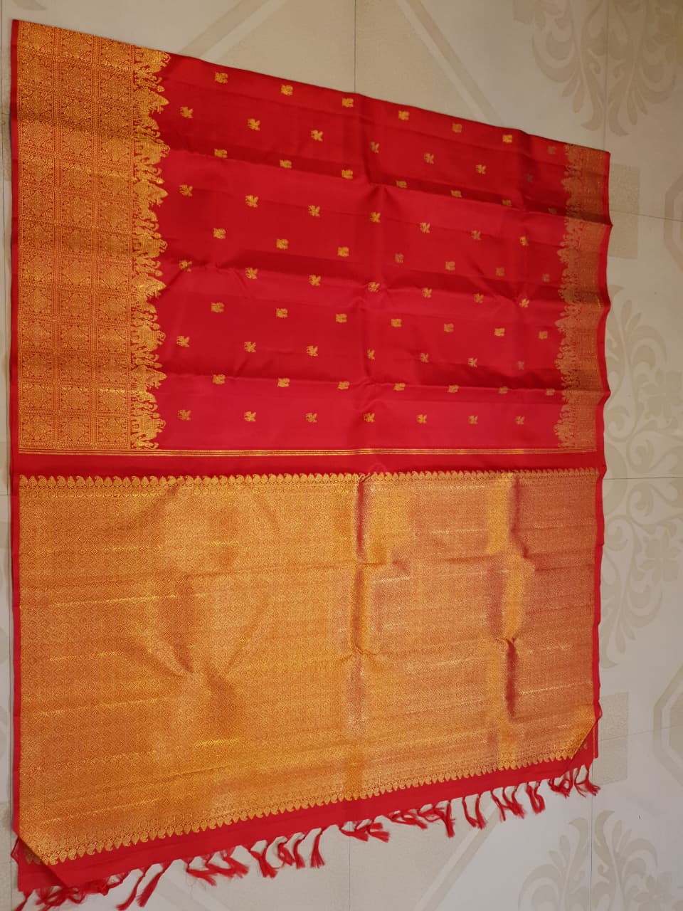 A close-up view of a premium 2G Kanjivaram pattu silk saree, highlighting the authentic Silk Mark tag, vibrant red fabric, and detailed gold zari work on the border and body.