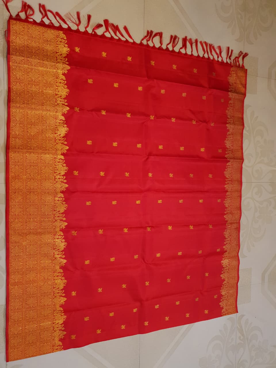 A close-up view of a premium 2G Kanjivaram pattu silk saree, highlighting the authentic Silk Mark tag, vibrant red fabric, and detailed gold zari work on the border and body.