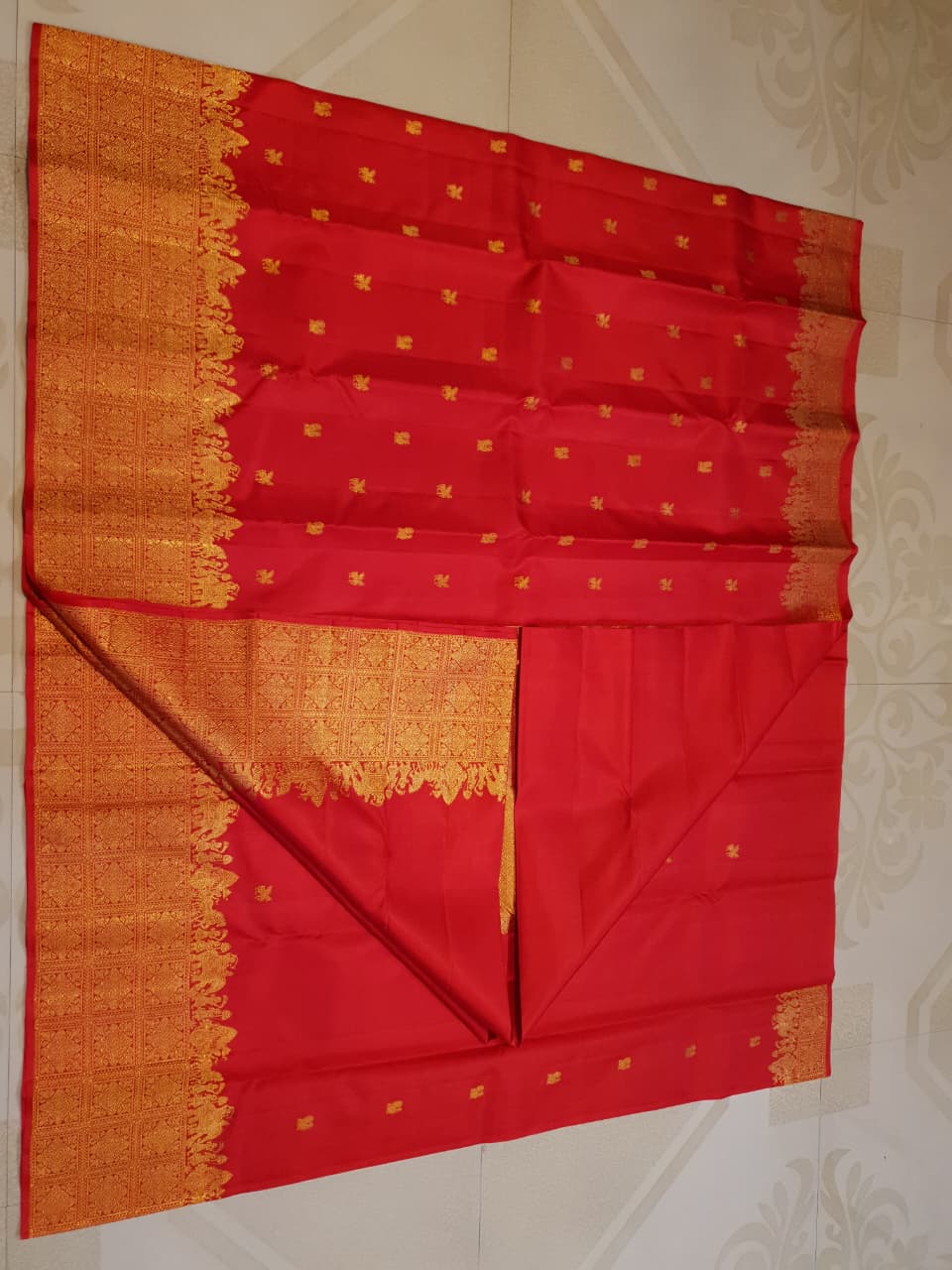 A close-up view of a premium 2G Kanjivaram pattu silk saree, highlighting the authentic Silk Mark tag, vibrant red fabric, and detailed gold zari work on the border and body.