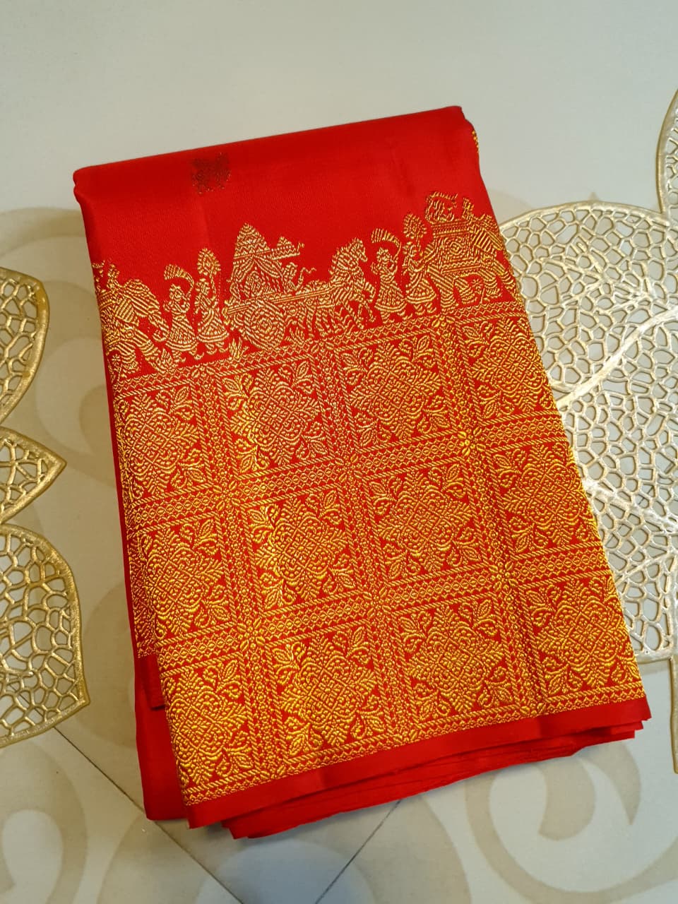 A close-up view of a premium 2G Kanjivaram pattu silk saree, highlighting the authentic Silk Mark tag, vibrant red fabric, and detailed gold zari work on the border and body.