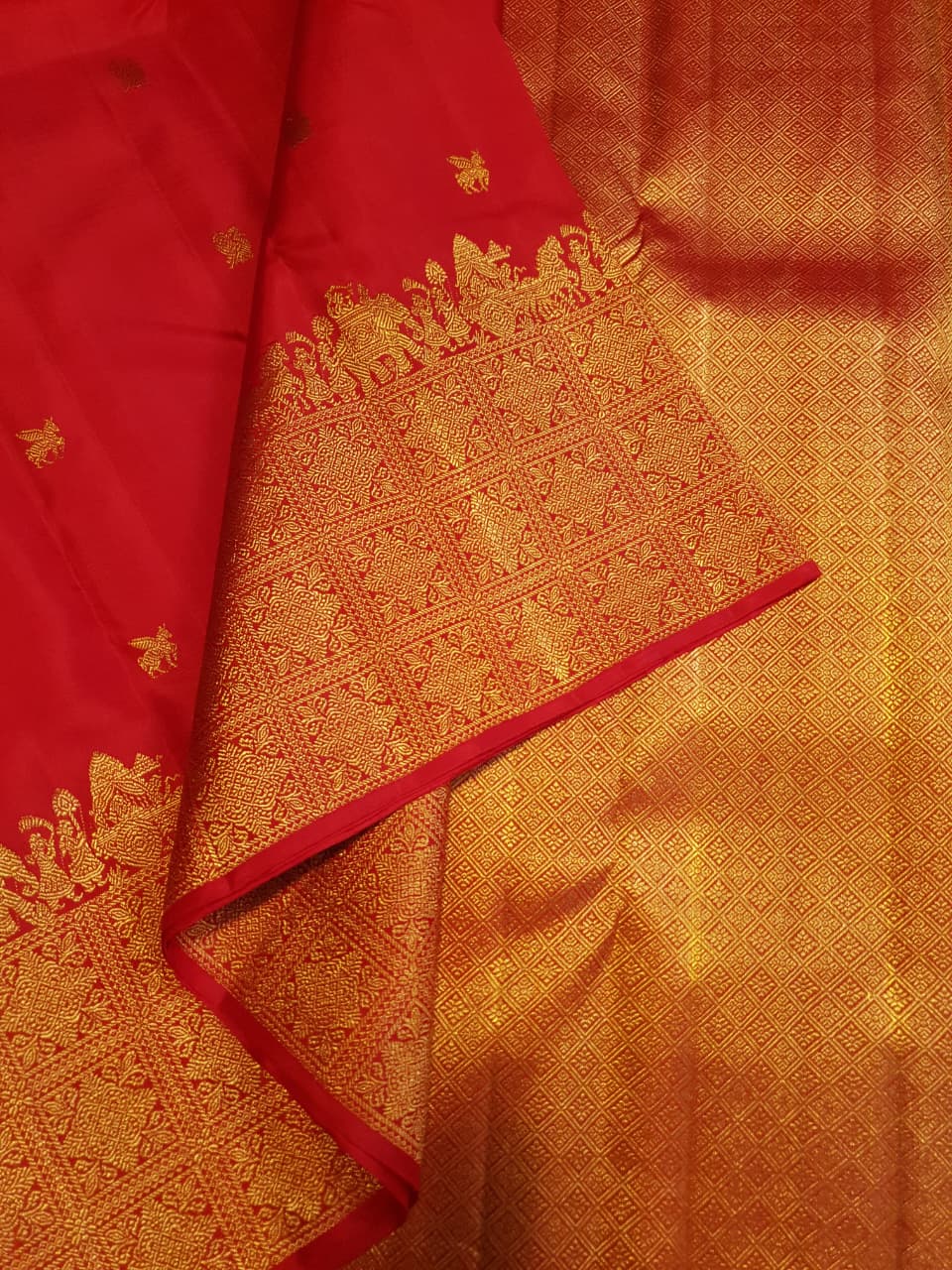 A close-up view of a premium 2G Kanjivaram pattu silk saree, highlighting the authentic Silk Mark tag, vibrant red fabric, and detailed gold zari work on the border and body.