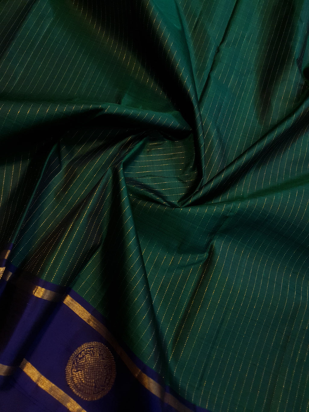 Bottle Green Kanjivaram silk saree featuring fine gold zari stripes and a contrasting royal blue border with large circular motifs.