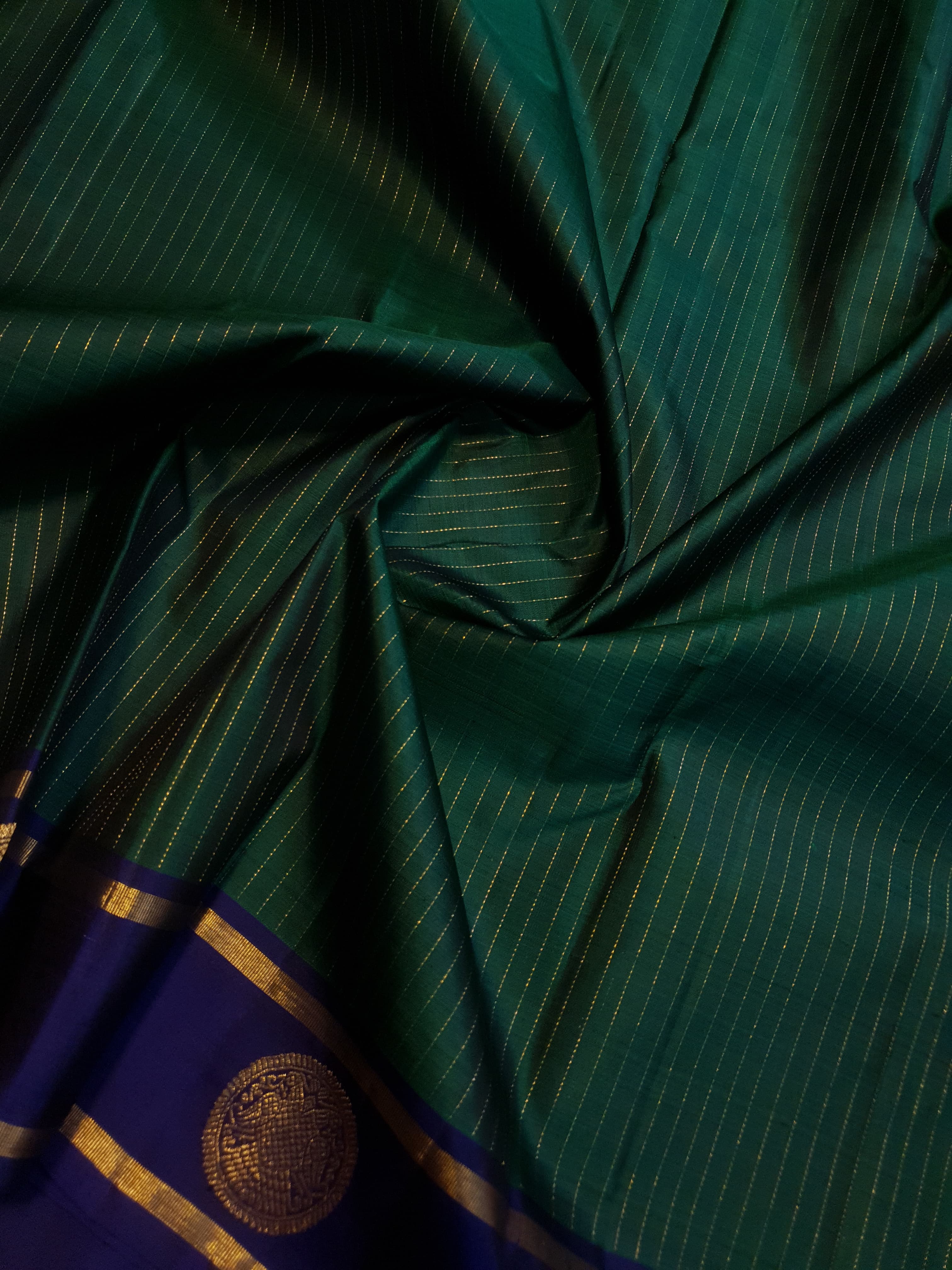 Bottle Green Kanjivaram silk saree featuring fine gold zari stripes and a contrasting royal blue border with large circular motifs.