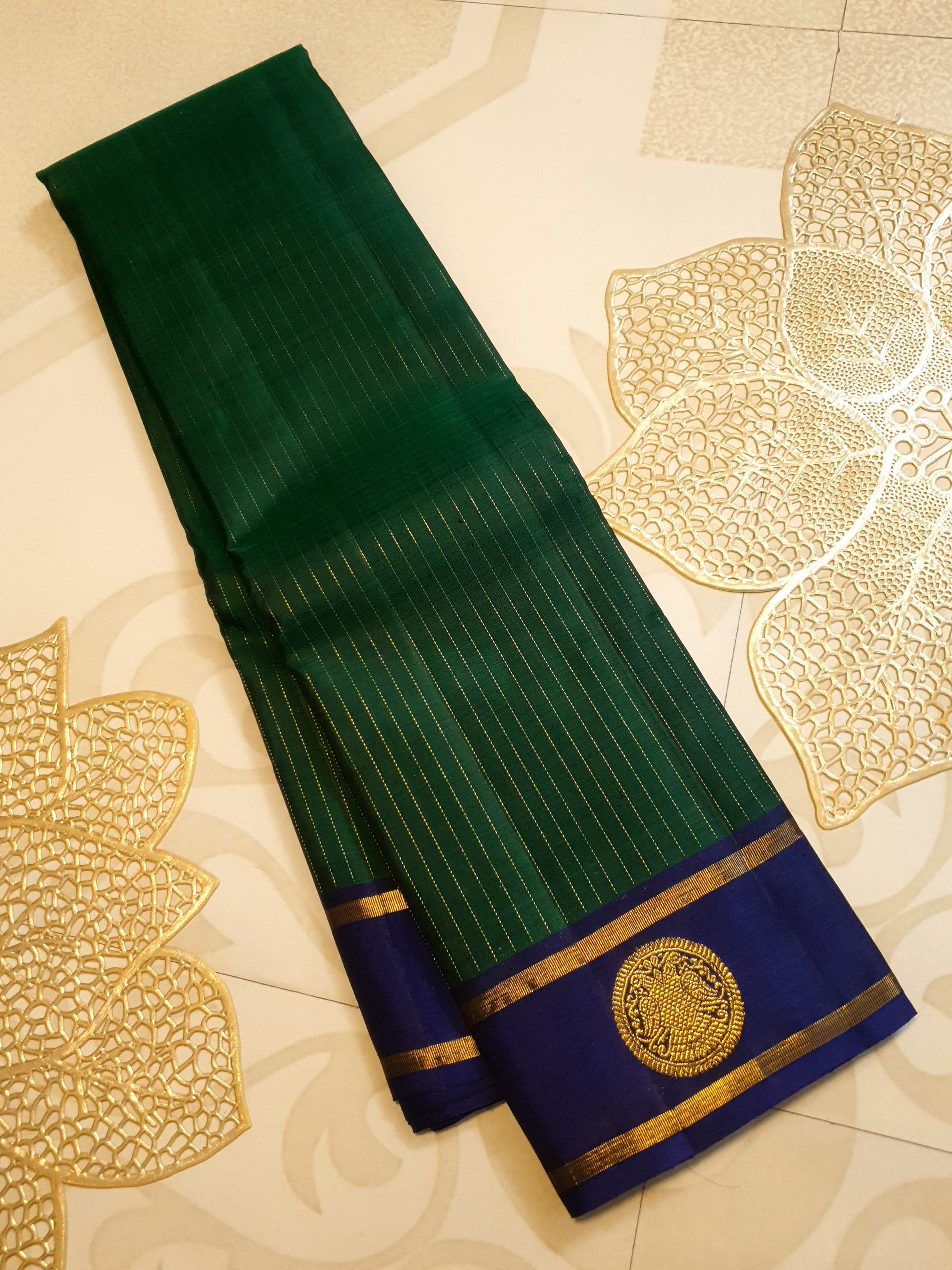 Bottle Green Kanjivaram silk saree featuring fine gold zari stripes and a contrasting royal blue border with large circular motifs.