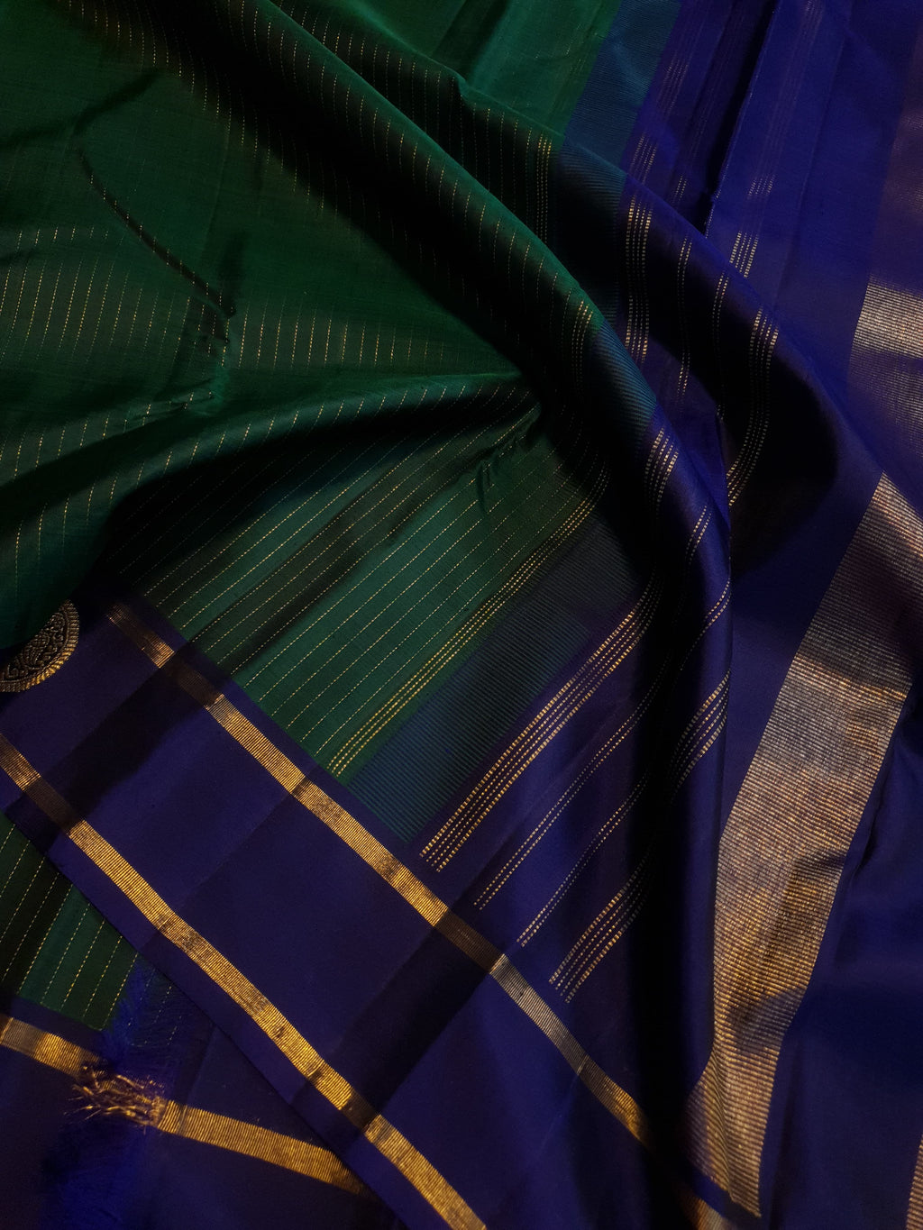 Bottle Green Kanjivaram silk saree featuring fine gold zari stripes and a contrasting royal blue border with large circular motifs.