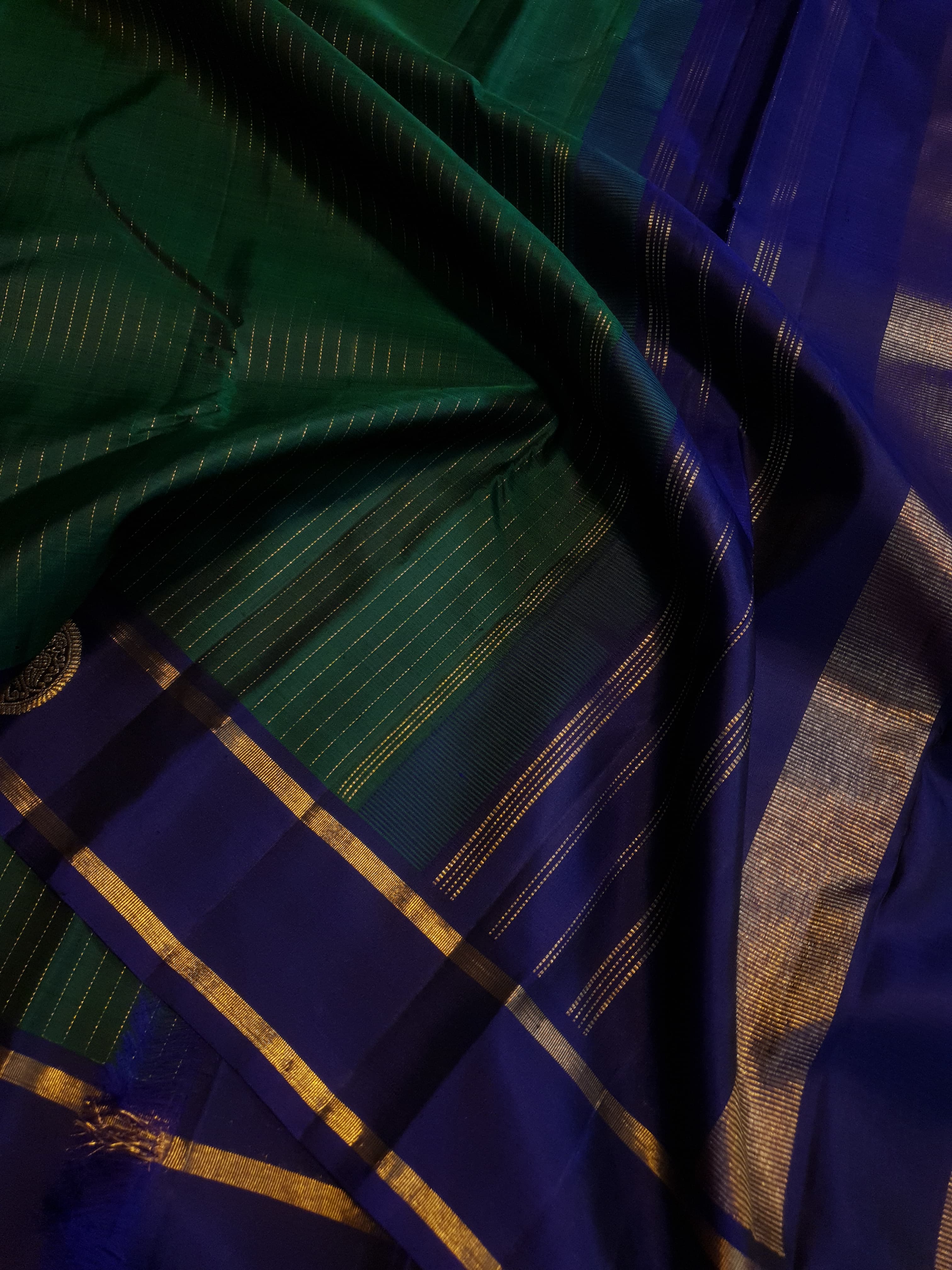 Bottle Green Kanjivaram silk saree featuring fine gold zari stripes and a contrasting royal blue border with large circular motifs.