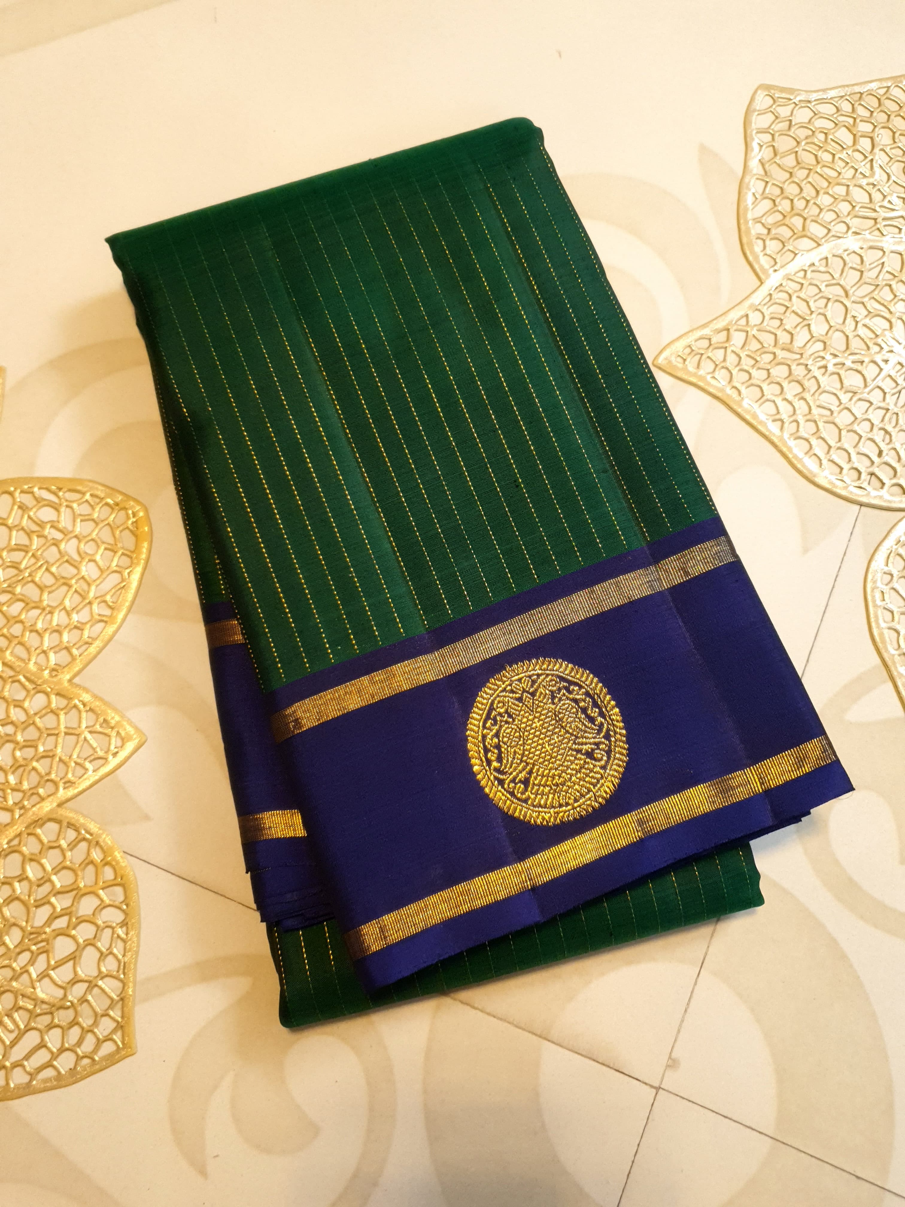 Bottle Green Kanjivaram silk saree featuring fine gold zari stripes and a contrasting royal blue border with large circular motifs.