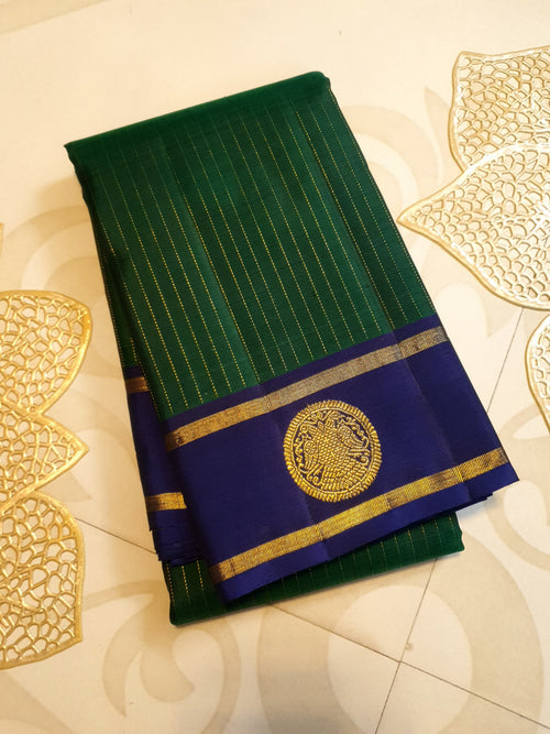 Bottle Green Kanjivaram silk saree featuring fine gold zari stripes and a contrasting royal blue border with large circular motifs.