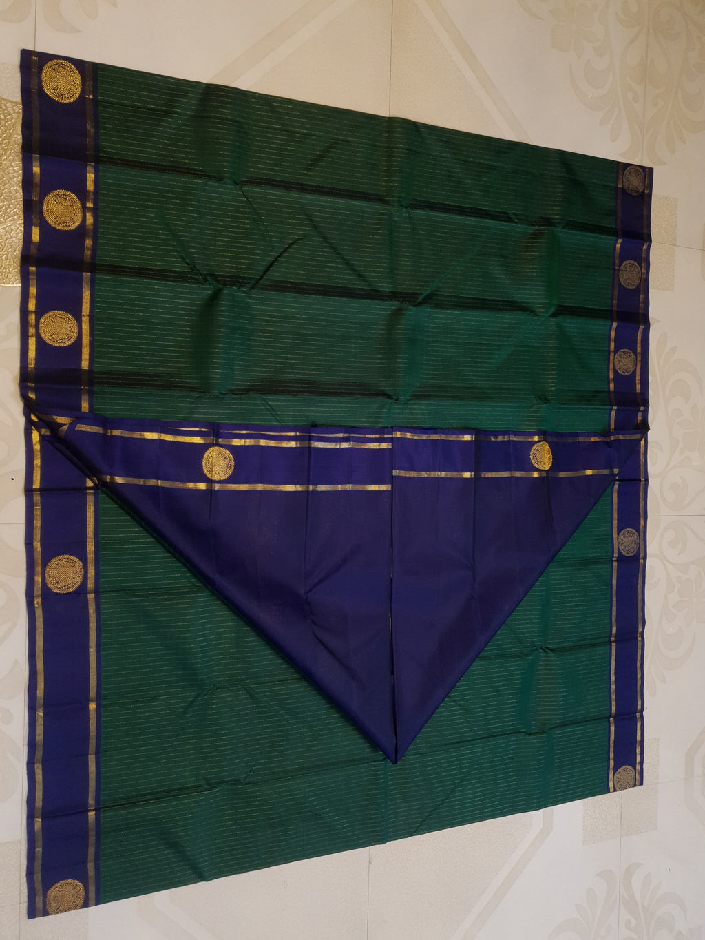Bottle Green Kanjivaram silk saree featuring fine gold zari stripes and a contrasting royal blue border with large circular motifs.