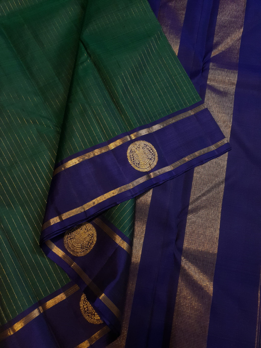 Bottle Green Kanjivaram silk saree featuring fine gold zari stripes and a contrasting royal blue border with large circular motifs.