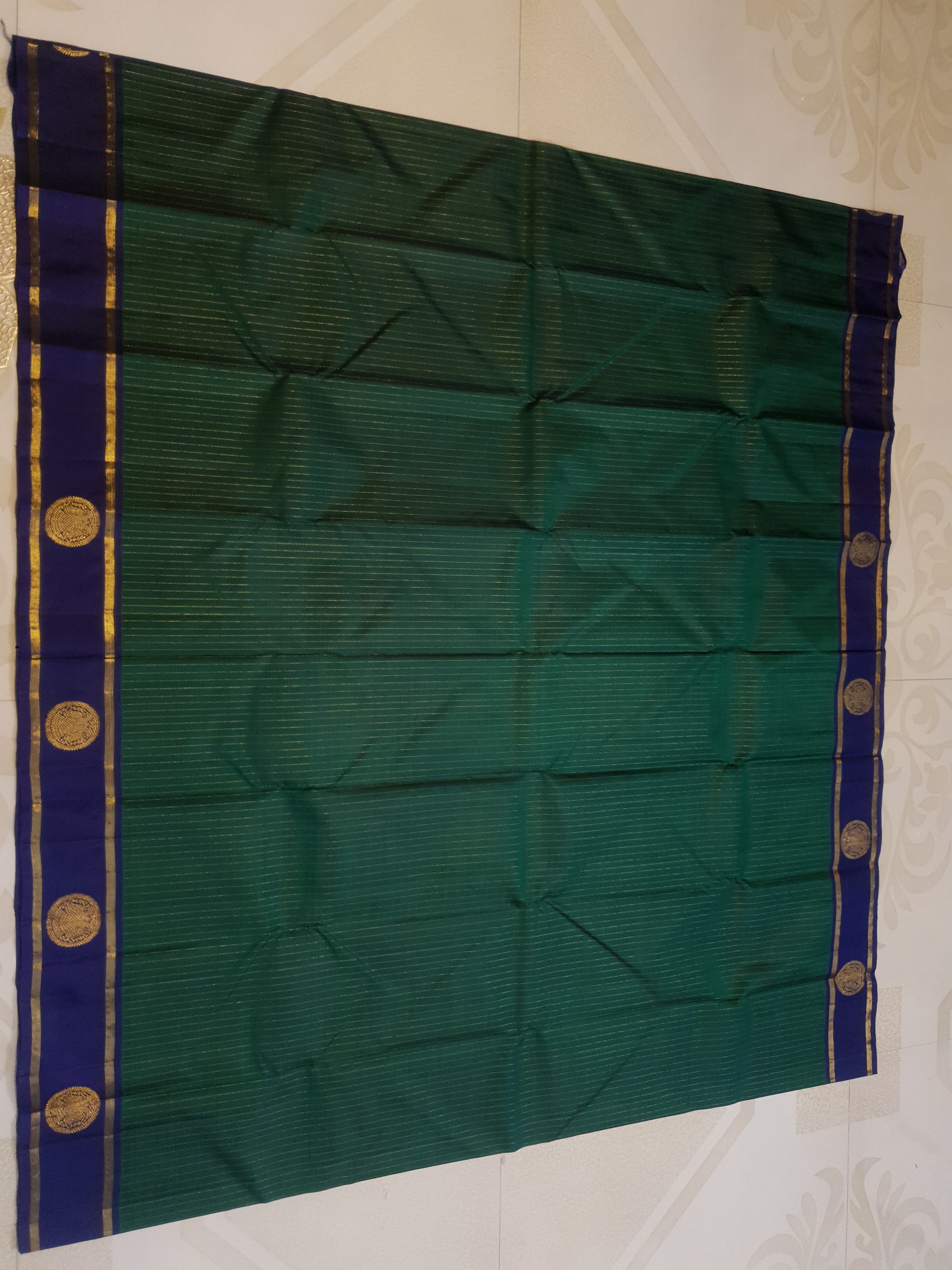 Bottle Green Kanjivaram silk saree featuring fine gold zari stripes and a contrasting royal blue border with large circular motifs.