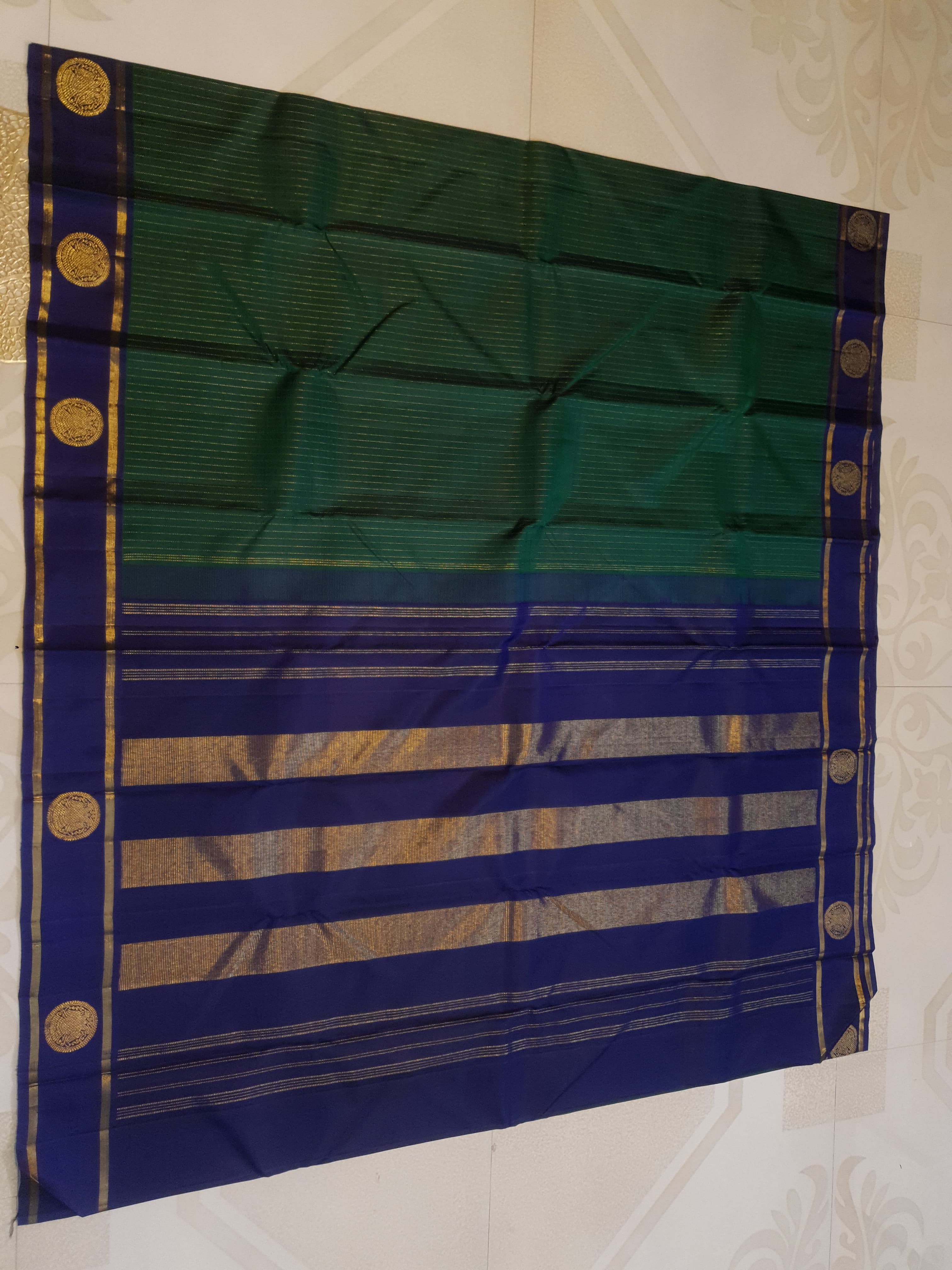 Bottle Green Kanjivaram silk saree featuring fine gold zari stripes and a contrasting royal blue border with large circular motifs.