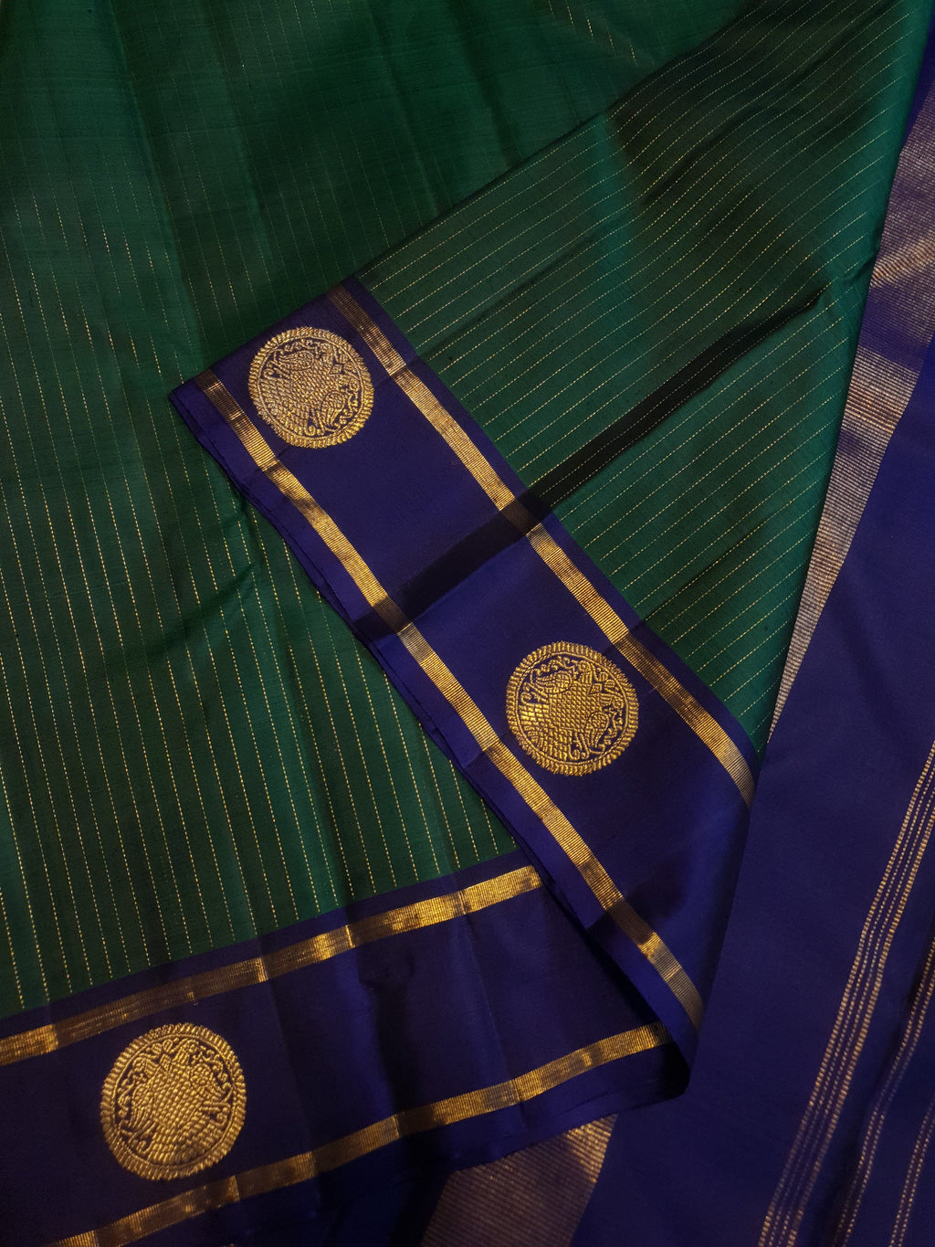 Bottle Green Kanjivaram silk saree featuring fine gold zari stripes and a contrasting royal blue border with large circular motifs.
