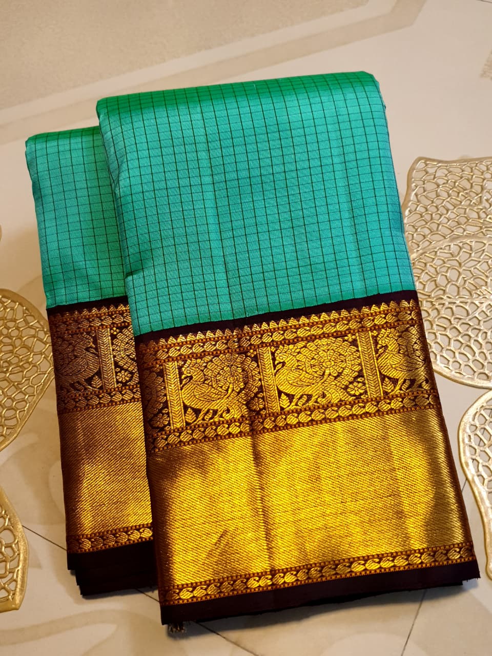 Sea Green Kanchipuram Handloom Silk Saree with small checks and a contrast purple border featuring gold zari peacock and floral patterns in a temple hallway.