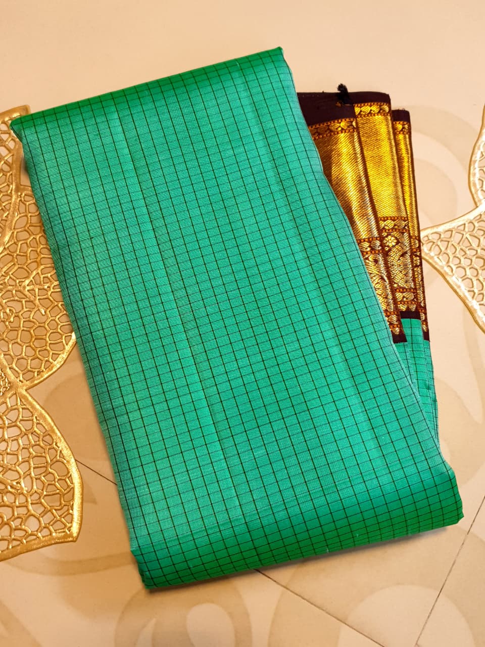 Sea Green Kanchipuram Handloom Silk Saree with small checks and a contrast purple border featuring gold zari peacock and floral patterns in a temple hallway.