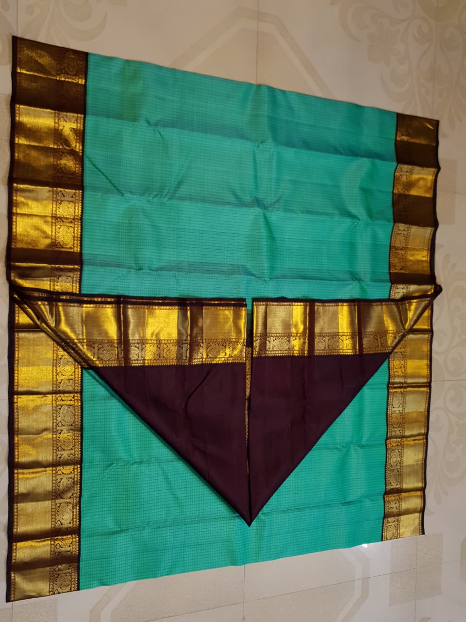 Sea Green Kanchipuram Handloom Silk Saree with small checks and a contrast purple border featuring gold zari peacock and floral patterns in a temple hallway.