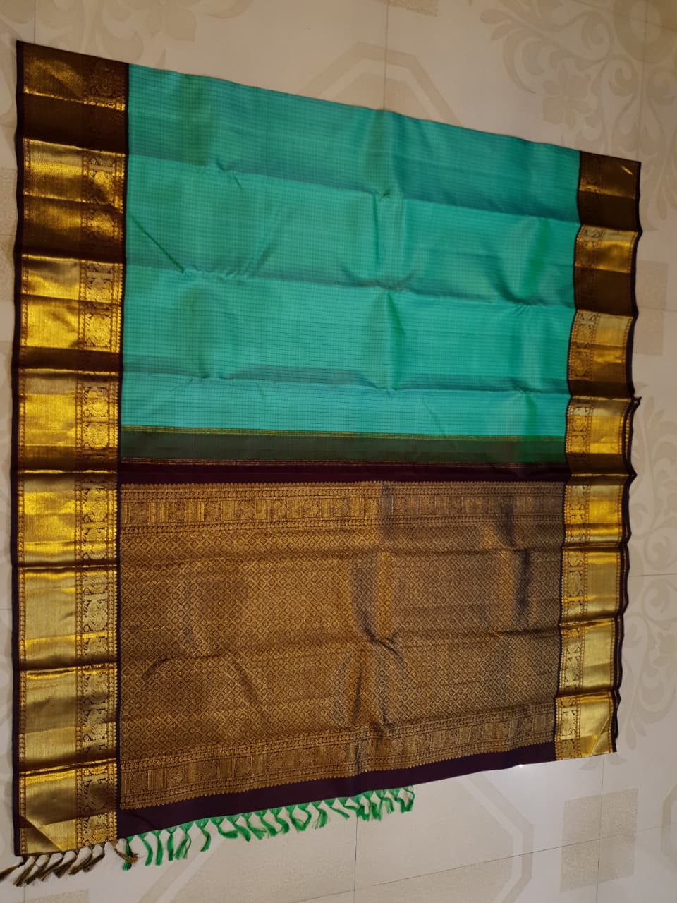 Sea Green Kanchipuram Handloom Silk Saree with small checks and a contrast purple border featuring gold zari peacock and floral patterns in a temple hallway.