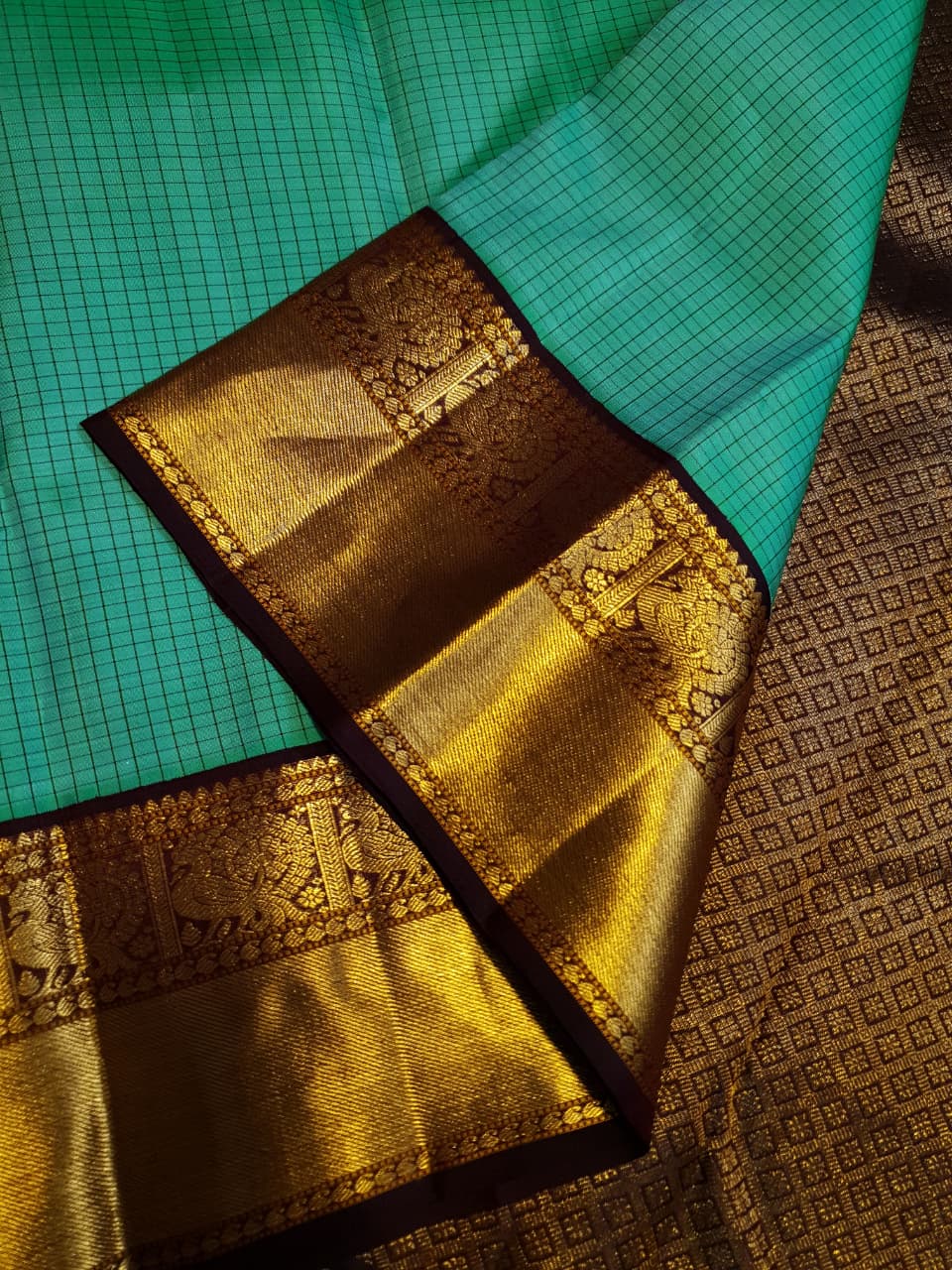 Sea Green Kanchipuram Handloom Silk Saree with small checks and a contrast purple border featuring gold zari peacock and floral patterns in a temple hallway.