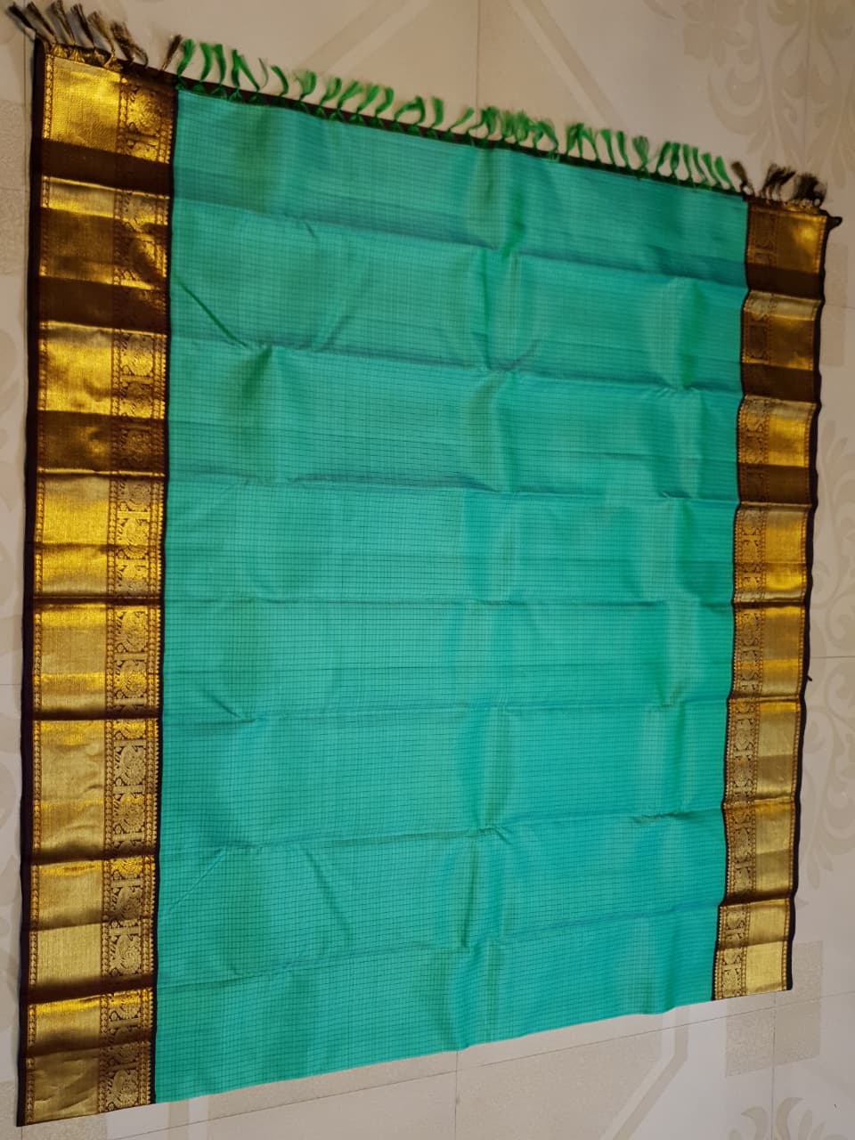 Sea Green Kanchipuram Handloom Silk Saree with small checks and a contrast purple border featuring gold zari peacock and floral patterns in a temple hallway.