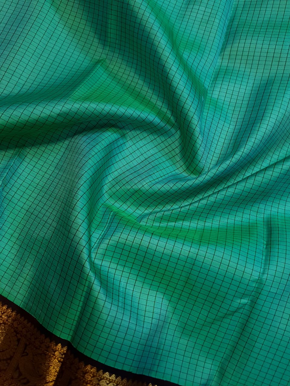 Sea Green Kanchipuram Handloom Silk Saree with small checks and a contrast purple border featuring gold zari peacock and floral patterns in a temple hallway.