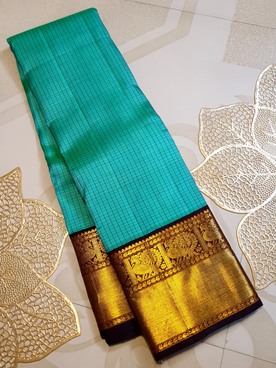 Sea Green Kanchipuram Handloom Silk Saree with small checks and a contrast purple border featuring gold zari peacock and floral patterns in a temple hallway.