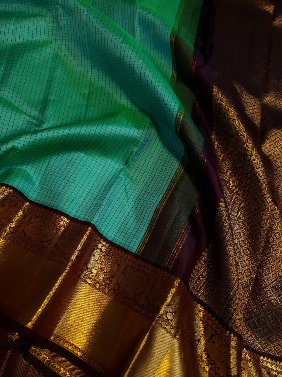 Sea Green Kanchipuram Handloom Silk Saree with small checks and a contrast purple border featuring gold zari peacock and floral patterns in a temple hallway.