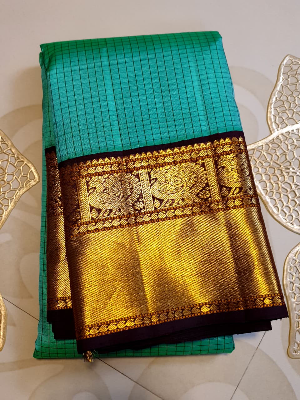 Sea Green Kanchipuram Handloom Silk Saree with small checks and a contrast purple border featuring gold zari peacock and floral patterns in a temple hallway.