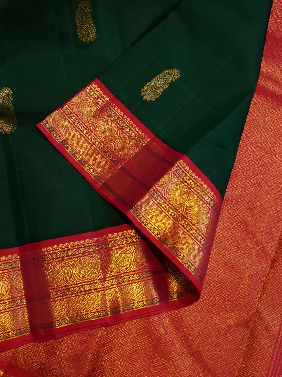 Bottle green Kanchipuram handloom Korvai silk saree, showcasing the intricate 2G gold zari motifs across the body, a vibrant contrasting pink and gold border, seamless Korvai interlocking craftsmanship, and an accompanying Silk Mark certification tag guaranteeing pure silk authenticity.