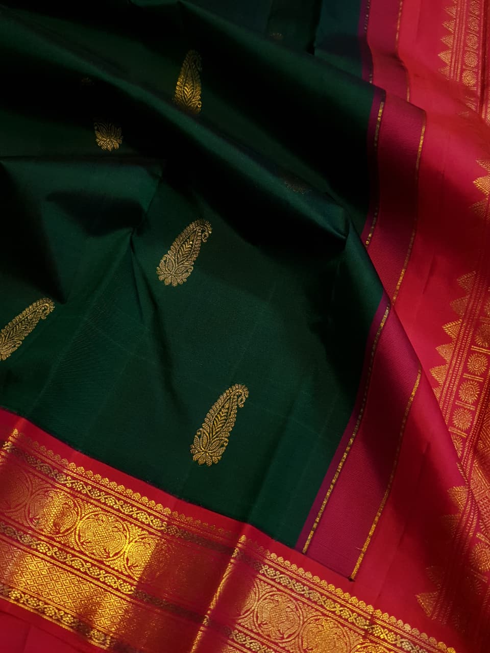 Bottle green Kanchipuram handloom Korvai silk saree, showcasing the intricate 2G gold zari motifs across the body, a vibrant contrasting pink and gold border, seamless Korvai interlocking craftsmanship, and an accompanying Silk Mark certification tag guaranteeing pure silk authenticity.