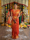 A model elegantly draped in a Chilly Red Kanchipuram Handloom 2G Gold Pattu Silk Saree with intricate floral brocade and a rich gold border, showcased in a traditional bridal setting.