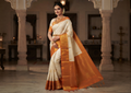A graceful model wearing a cream and orange Kanchipuram handloom 2G gold korvai silk saree featuring traditional gold zari weaving and classic paisley buttis.
