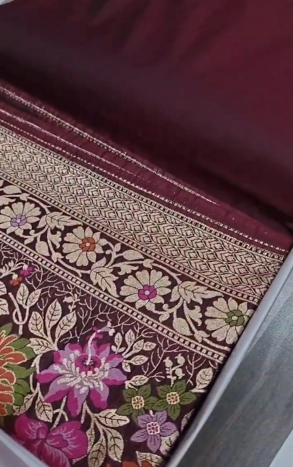 A deep wine-colored Banarasi semi Katan silk saree with a minimalist plain body, intricate Tilfi Meenakari floral borders, and a heavy gold zari blouse.