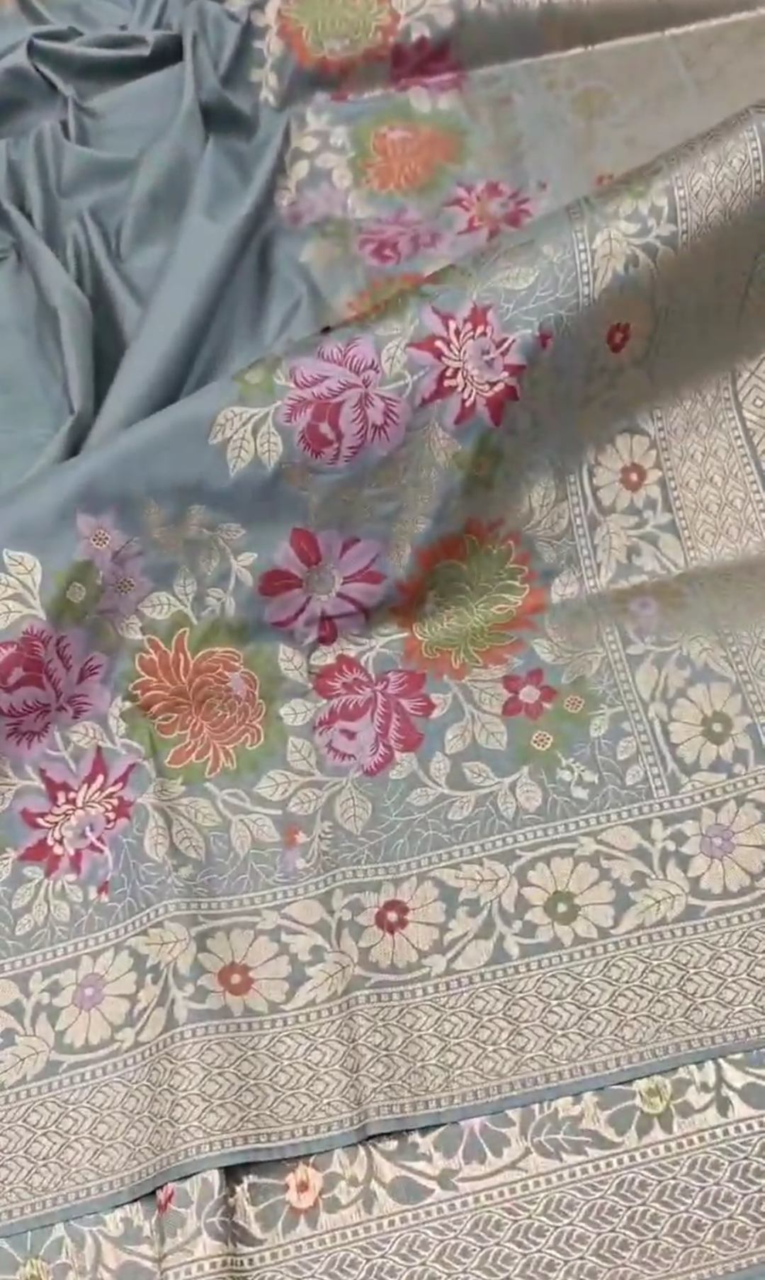 A serene powder blue Banarasi semi Katan silk saree with a plain body, a multi-colored Tilfi Meenakari floral border, and a matching heavy brocade blouse.
