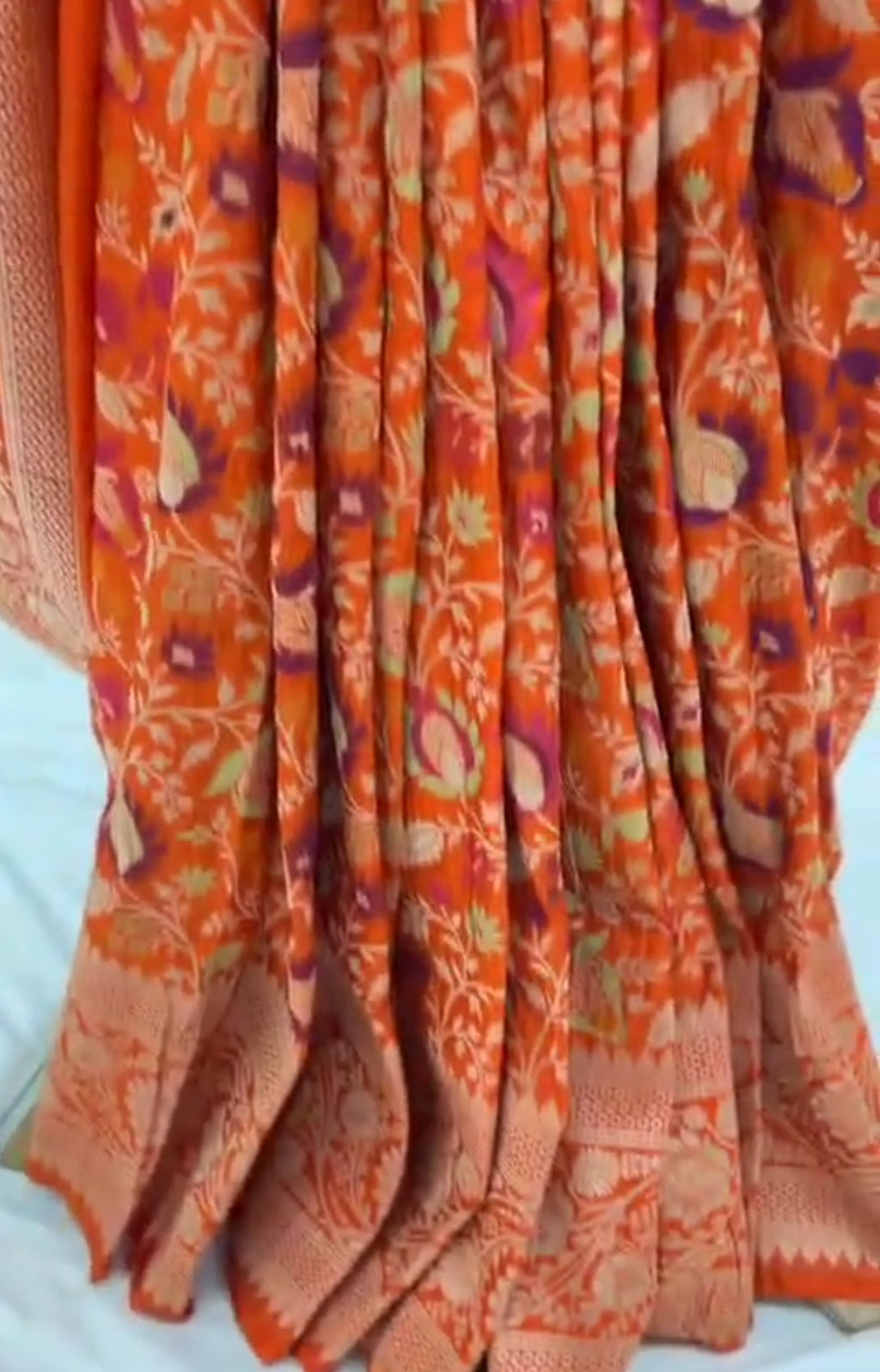A vibrant orange Banarasi Katan silk saree with multi-colored Tilfi Meenakari floral motifs and an elaborate gold zari border.