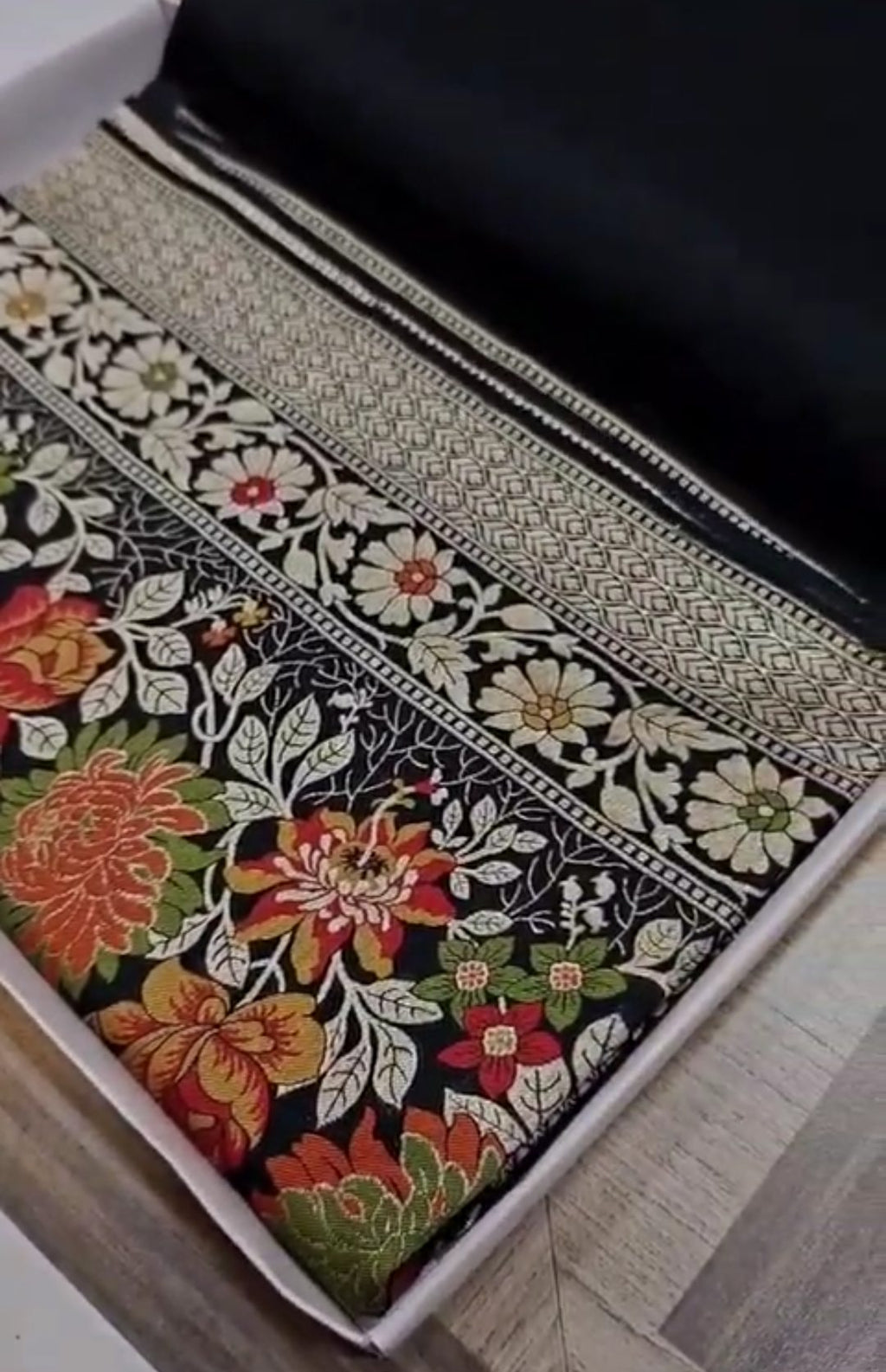 A majestic black Banarasi semi Katan silk saree with a plain body, vibrant three-colored Tilfi Meenakari floral borders, and an ornate gold zari blouse.