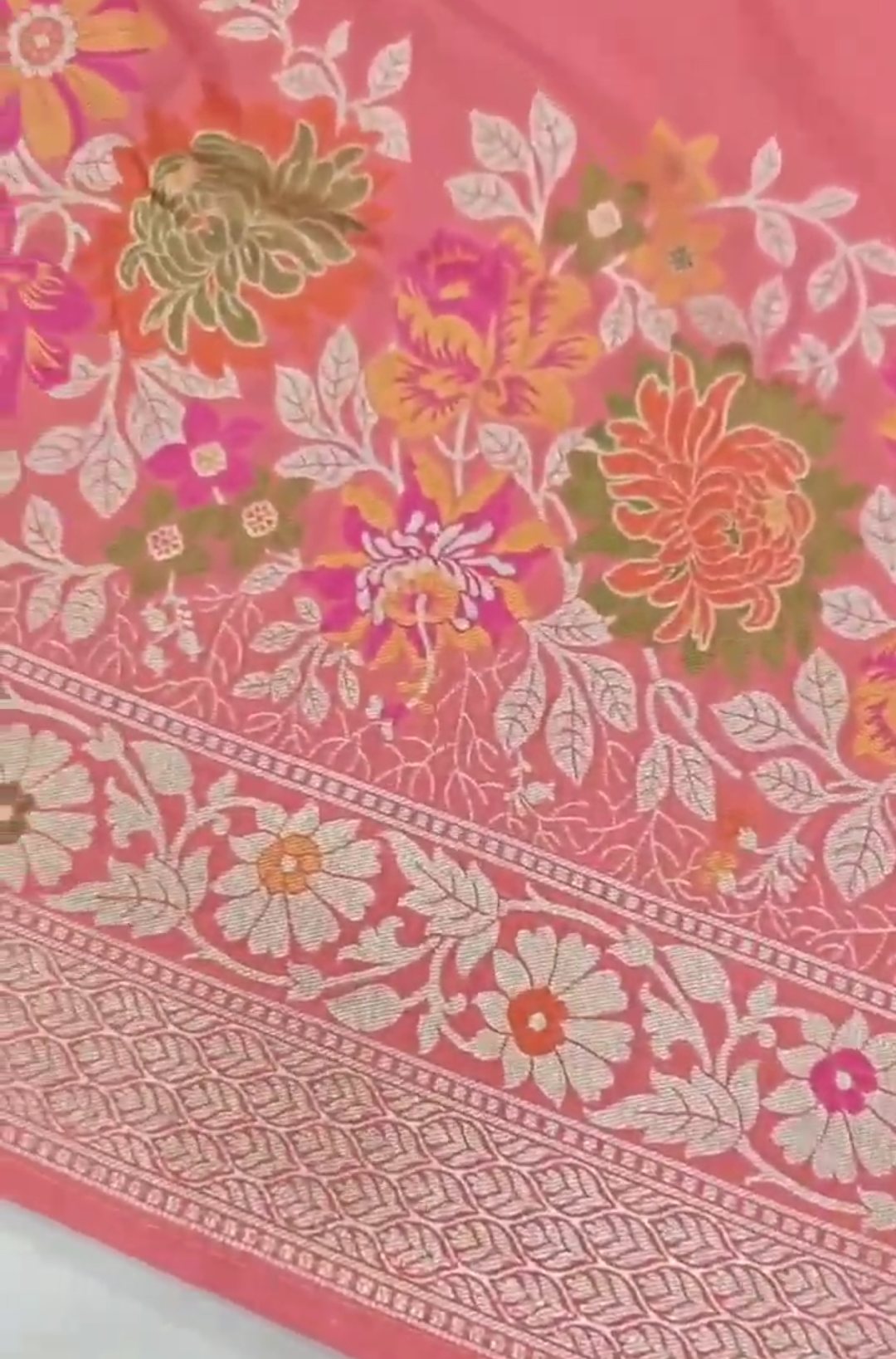A soft peach Banarasi semi Katan silk saree with a plain body, featuring a multi-colored Tilfi Meenakari floral border and a matching full brocade blouse piece.