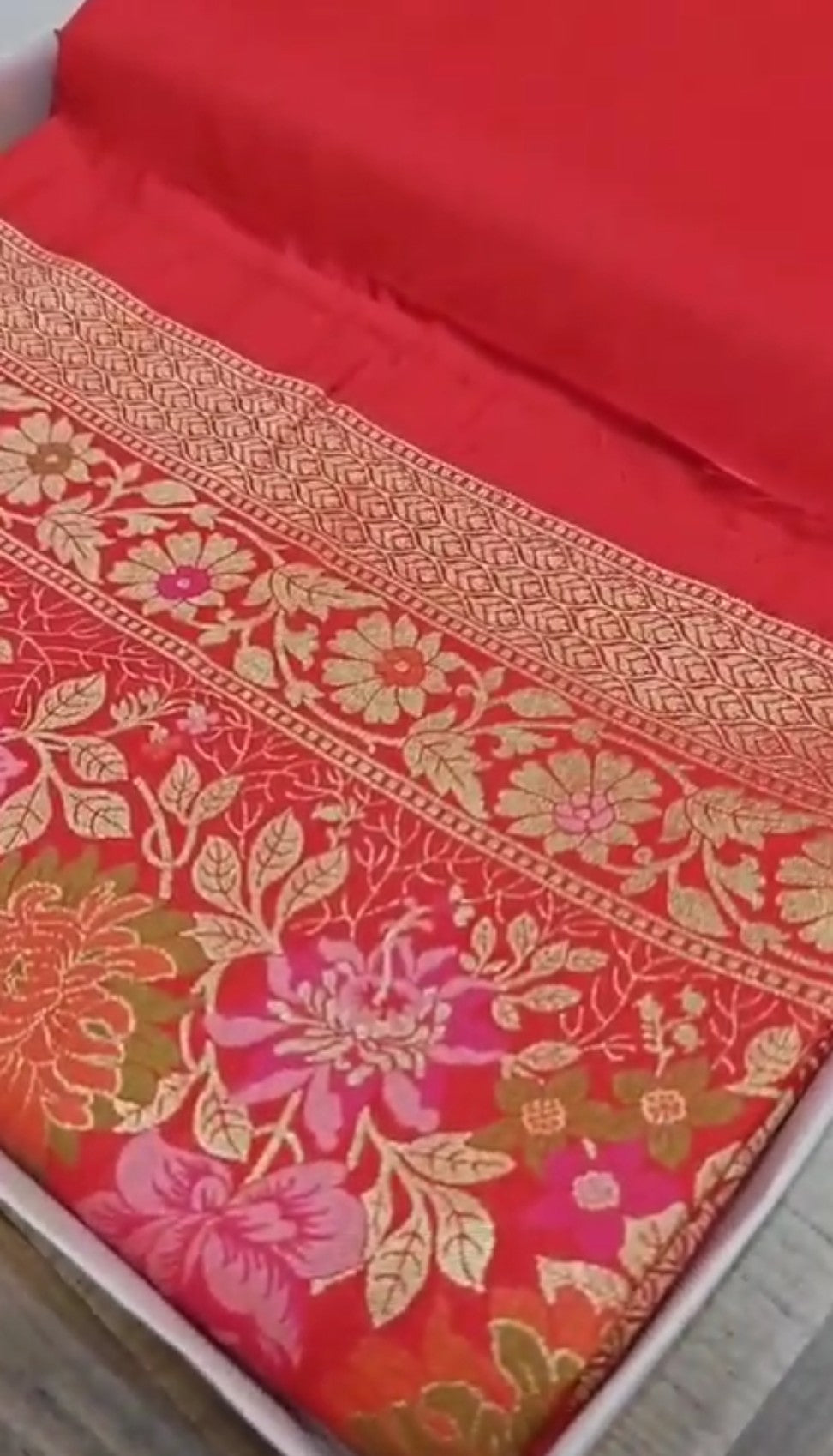 A bright bridal red Banarasi semi Katan silk saree with a minimalist plain body, intricate Tilfi Meenakari floral borders, and a heavy gold zari brocade blouse.