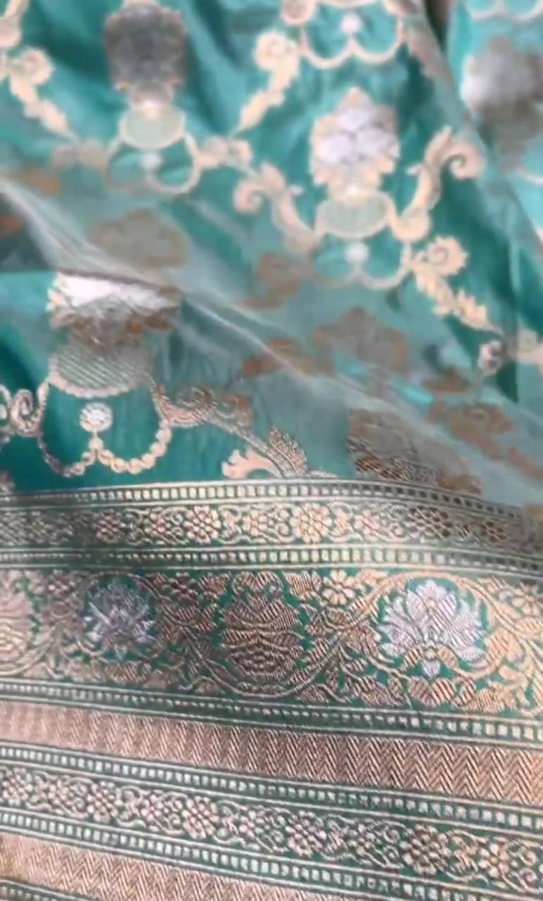 A vibrant turquoise Banarasi Katan silk saree with hand-woven Sona Rupa gold and silver zari floral motifs and an ornate border.