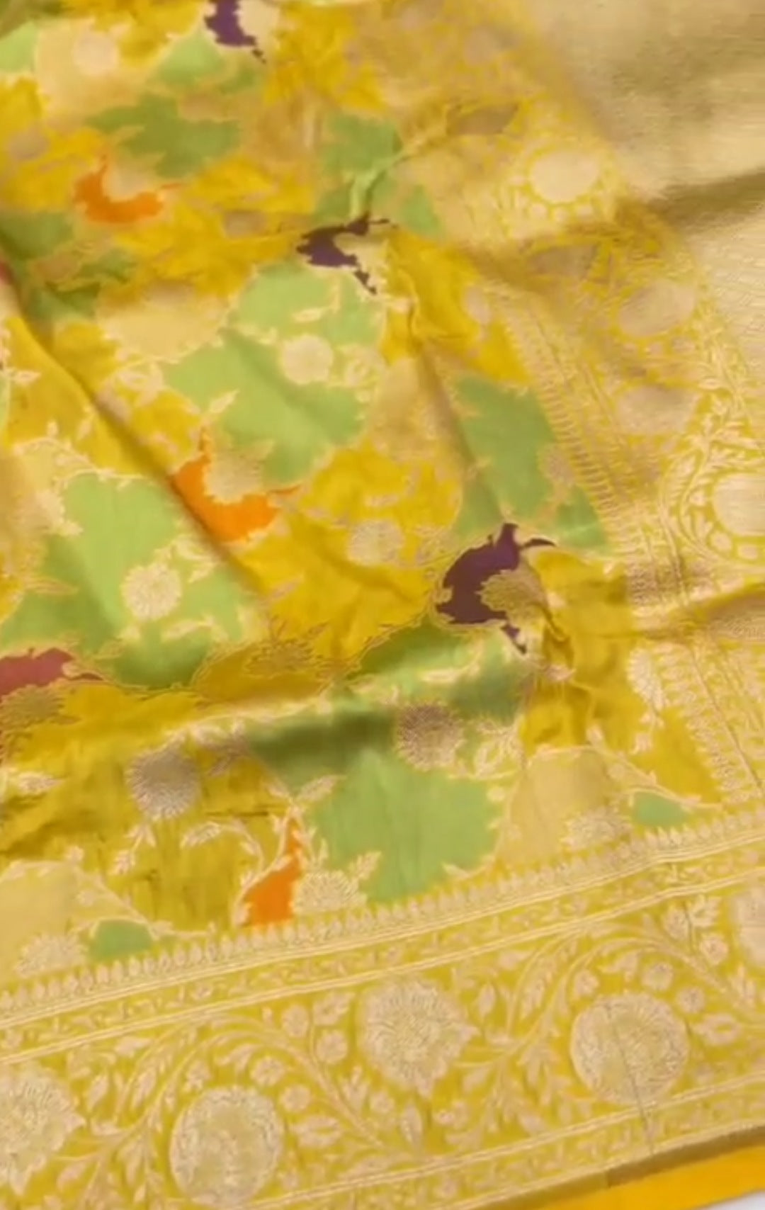 A luminous golden yellow Banarasi Katan silk saree with hand-woven Rangkaat diagonal patterns and vibrant multi-colored Meenakari floral vines.
